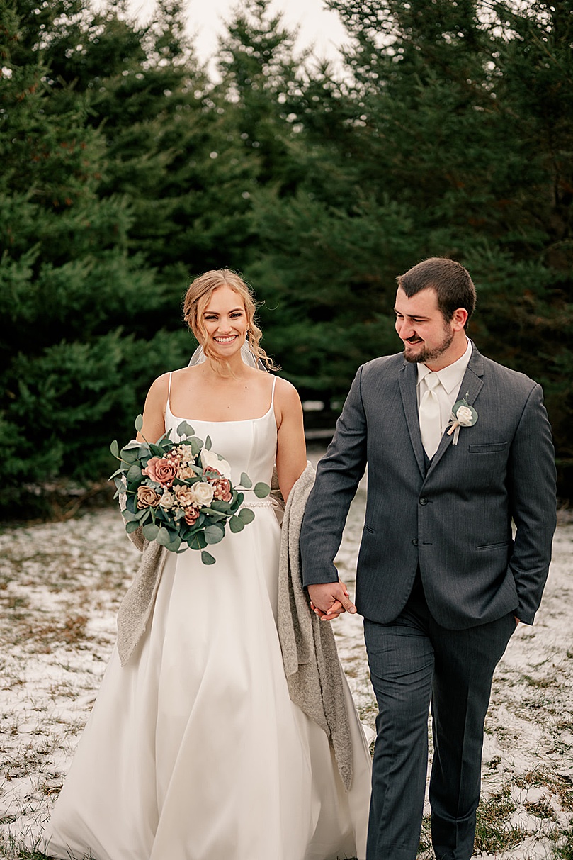 newlyweds walk in front of pine trees in snow by Rule Creative Co