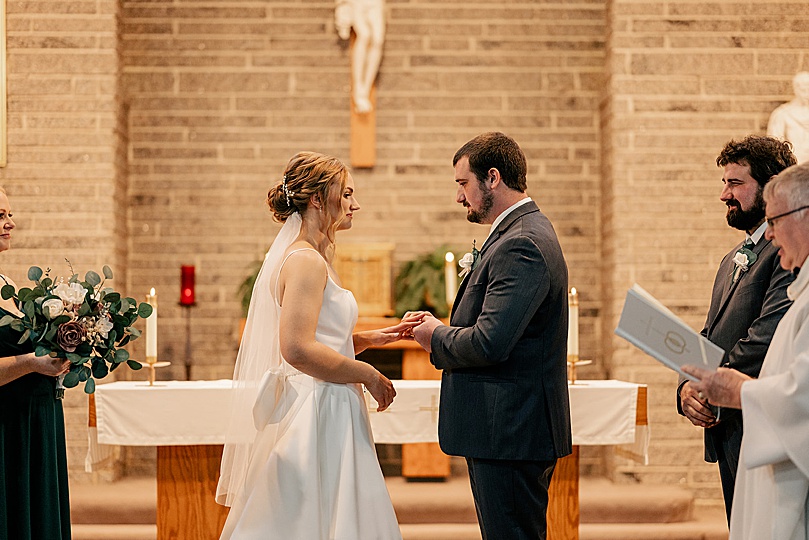 man puts ring on woman's finger at alter by Minnesota wedding photographer