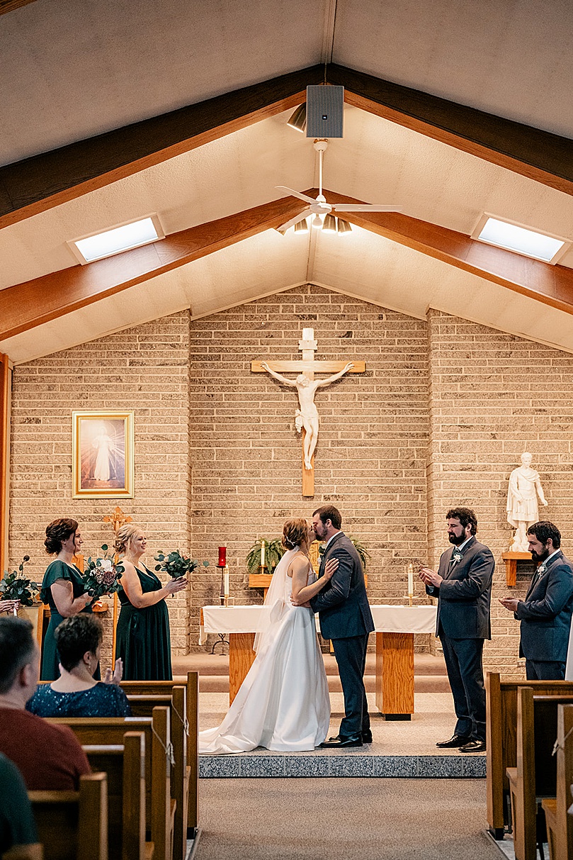 bride and groom share first kiss at alter for Romantic Winter Wedding in Brooten