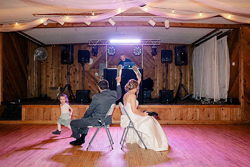 newlyweds play game on dance floor in back to back chairs by Rule Creative Co