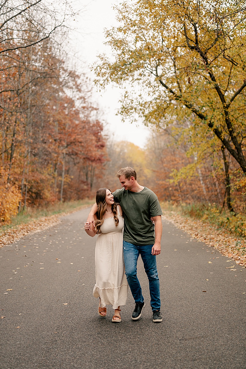 blonde man walks with his girl in white dress during rainy day engagement photos