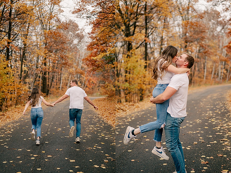 man holds up his bride to be on the road for rainy day engagement photos