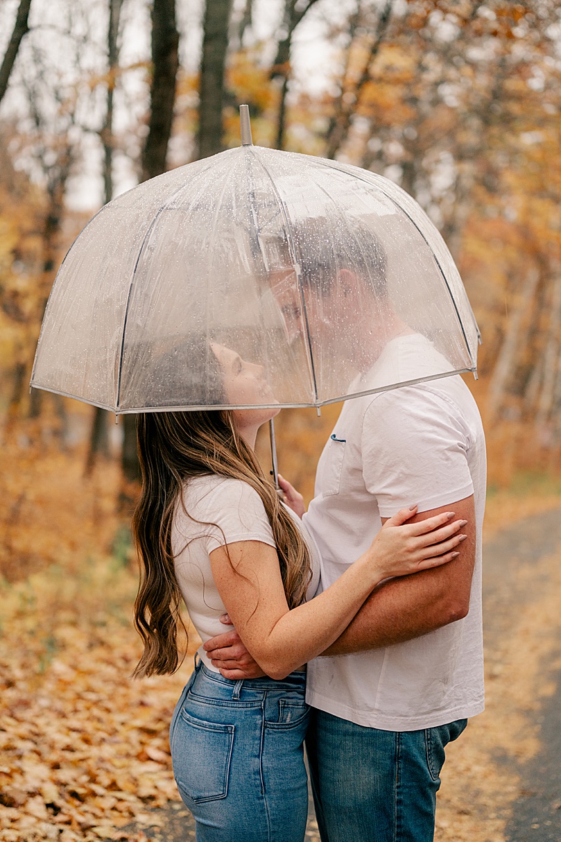 engaged couple embrace under clear umbrella by Rule Creative Co