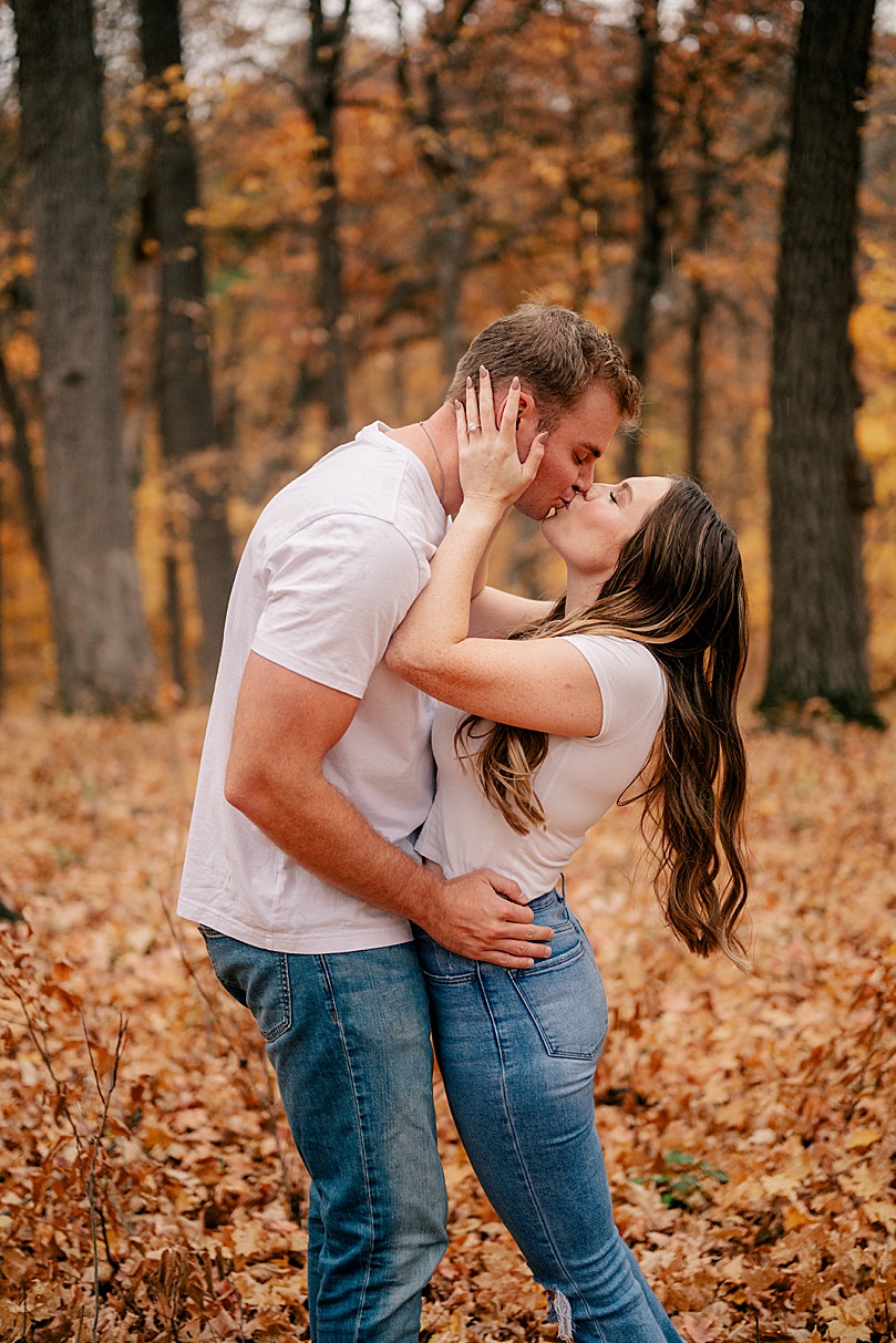 brunette woman kisses her man in fall trees by Minnesota wedding photographer