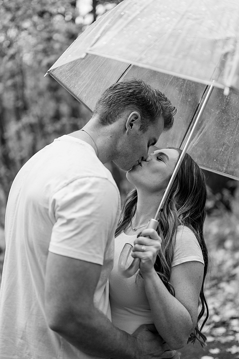 engaged couple kiss under umbrella for rainy day engagement photos