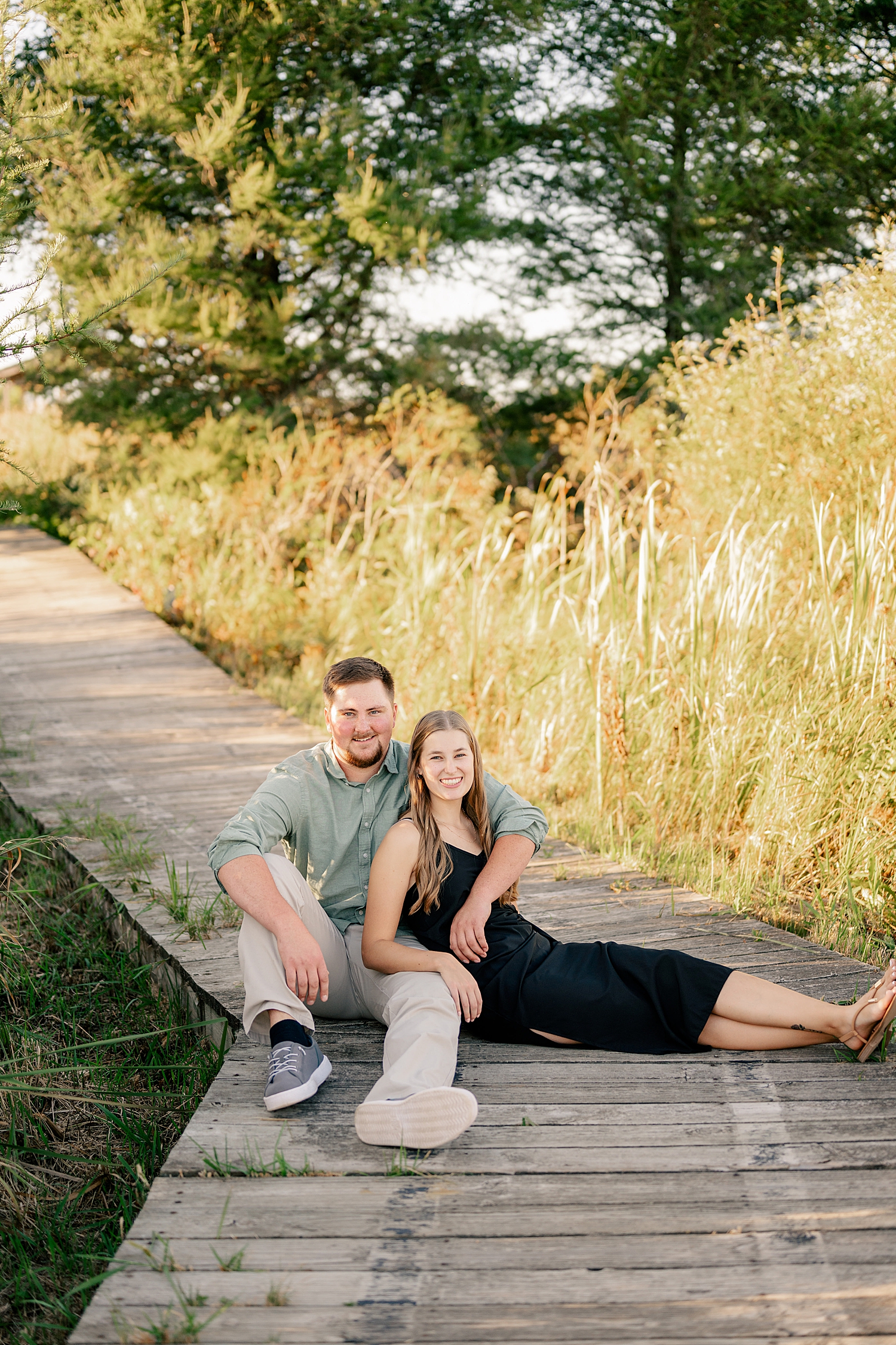 engaged couple sitting on boardwalk  by Rule Creative Co