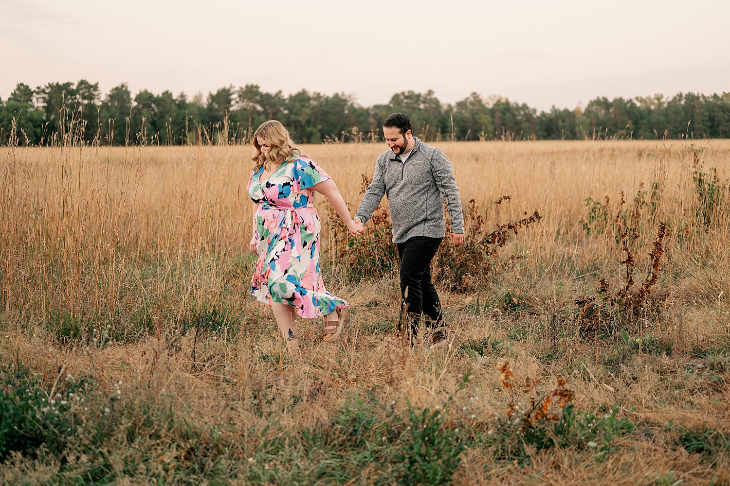 man and woman walk through a field at golden hour by Minnesota wedding photographer 