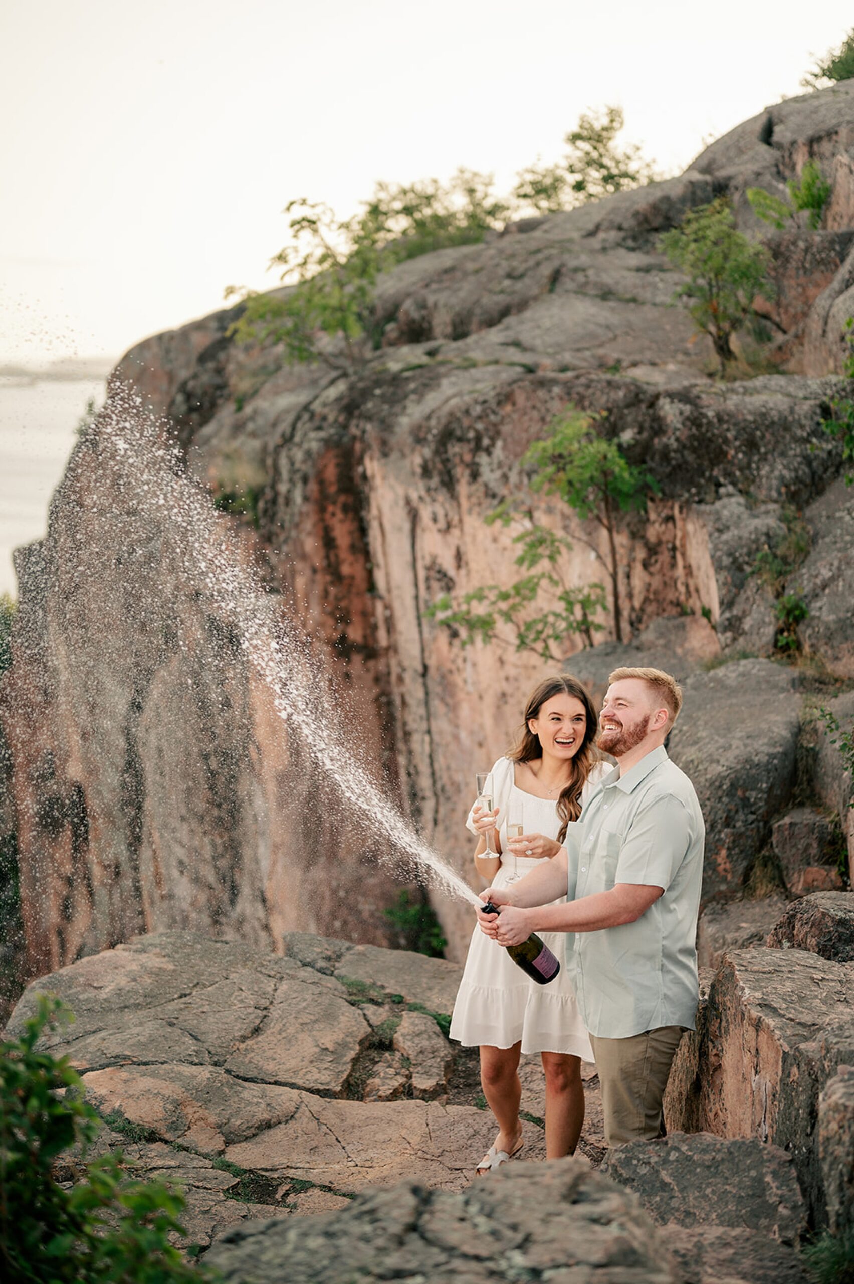 Couple sprays champagne in the mountains showing engagement session prop ideas