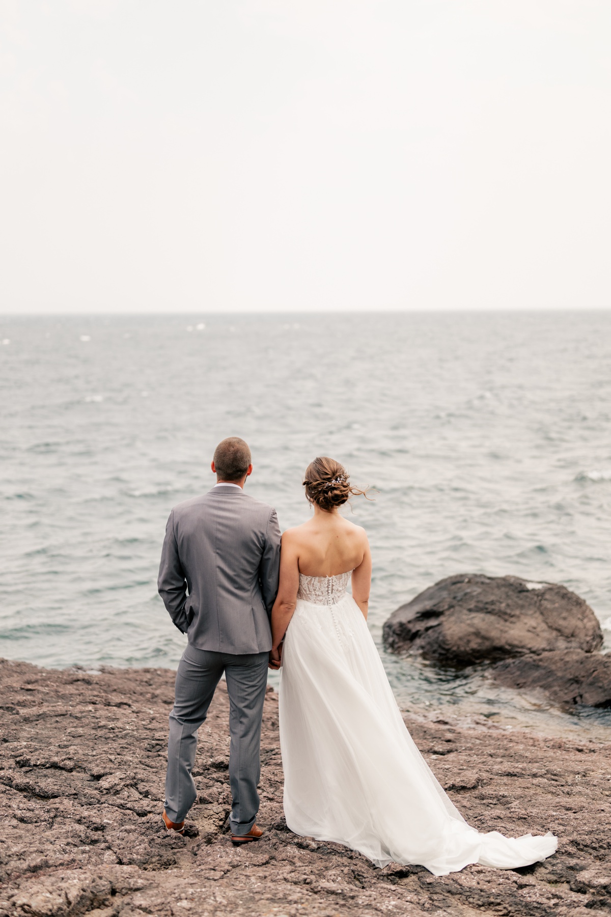Bride and groom stand on rocky shore during a North Shore Elopement