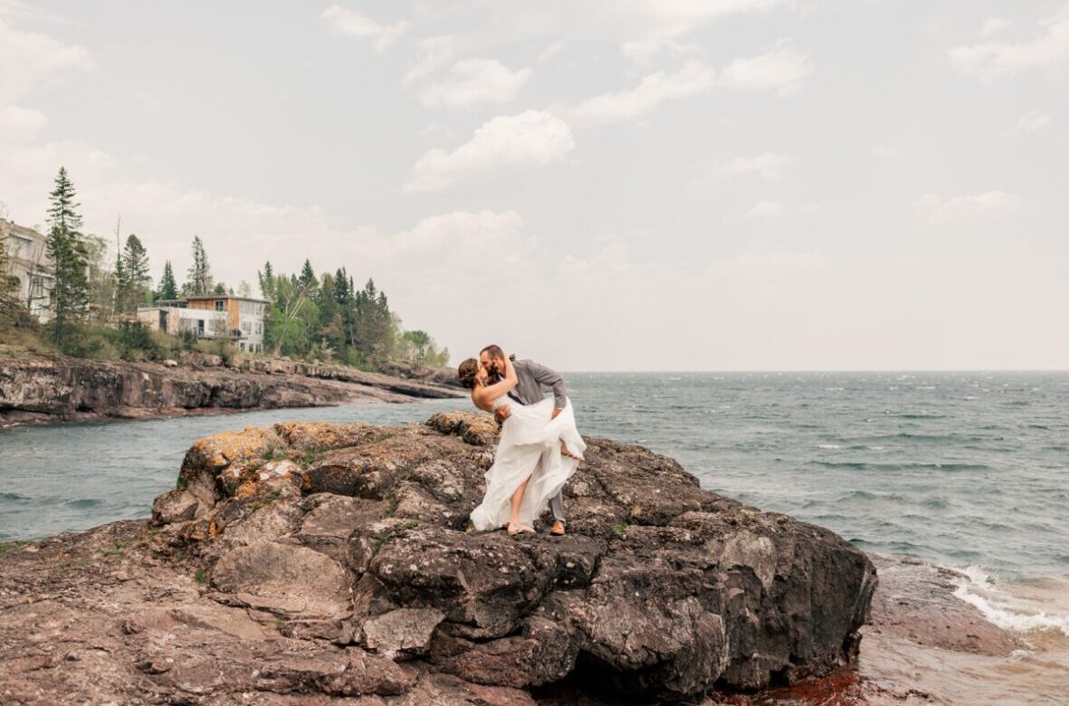Couple stands on rocky bluff kissing during North Shore Elopement
