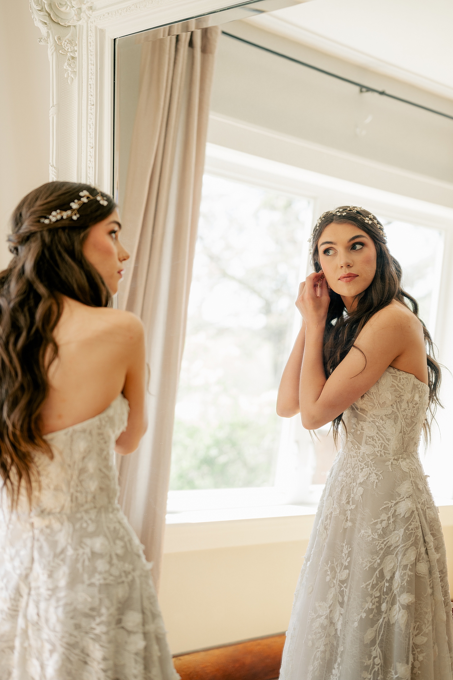woman in white lace gown adjusts earring in mirror by Minnesota wedding photographer