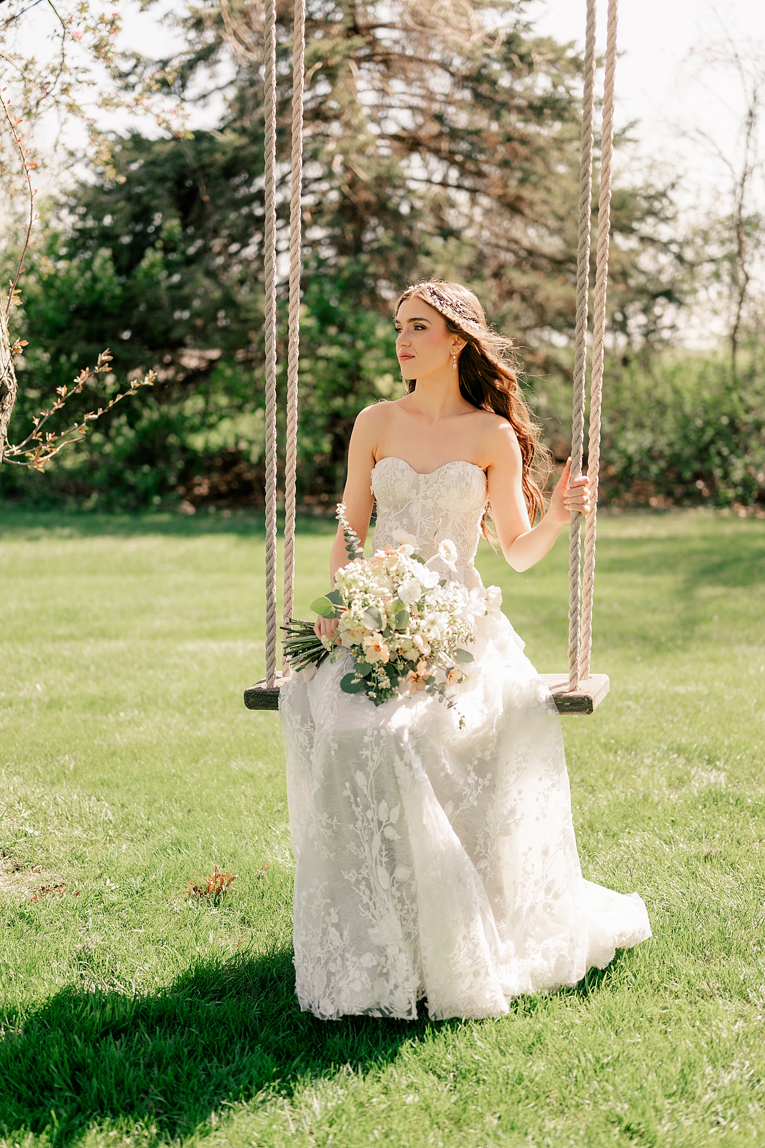 bride sits on swing in garden, holding florals at The Cottage Farmhouse