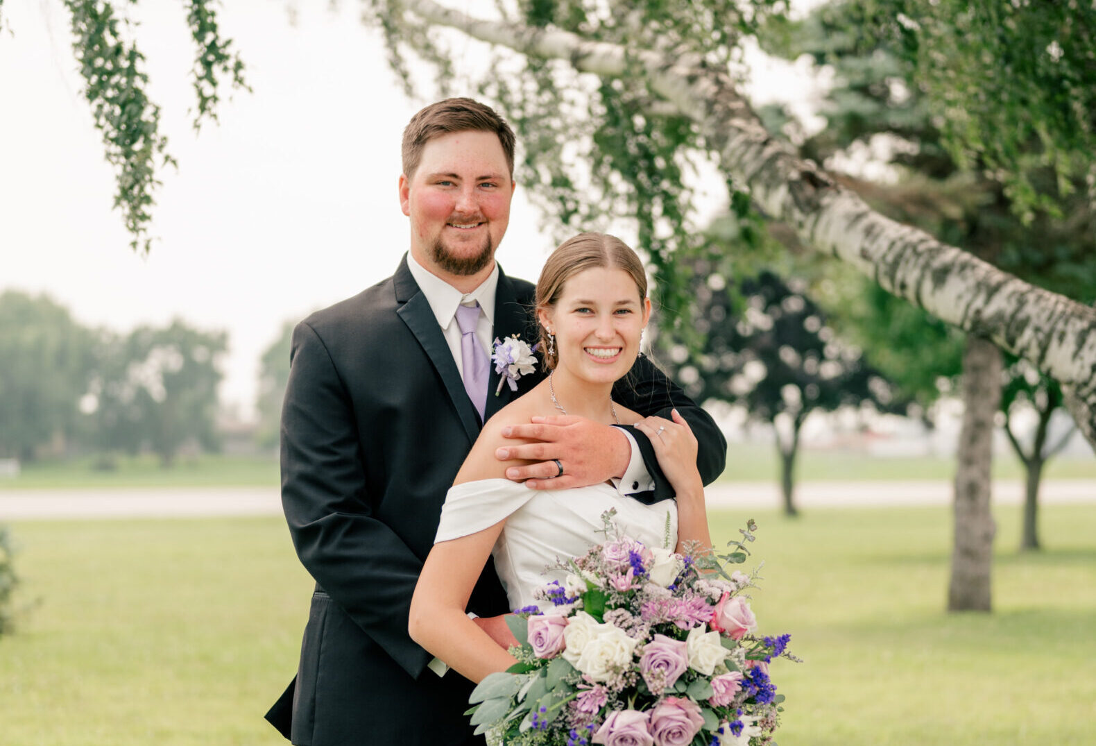 Bride and groom hold each other under breezy tree branches by Rule Creative Co.