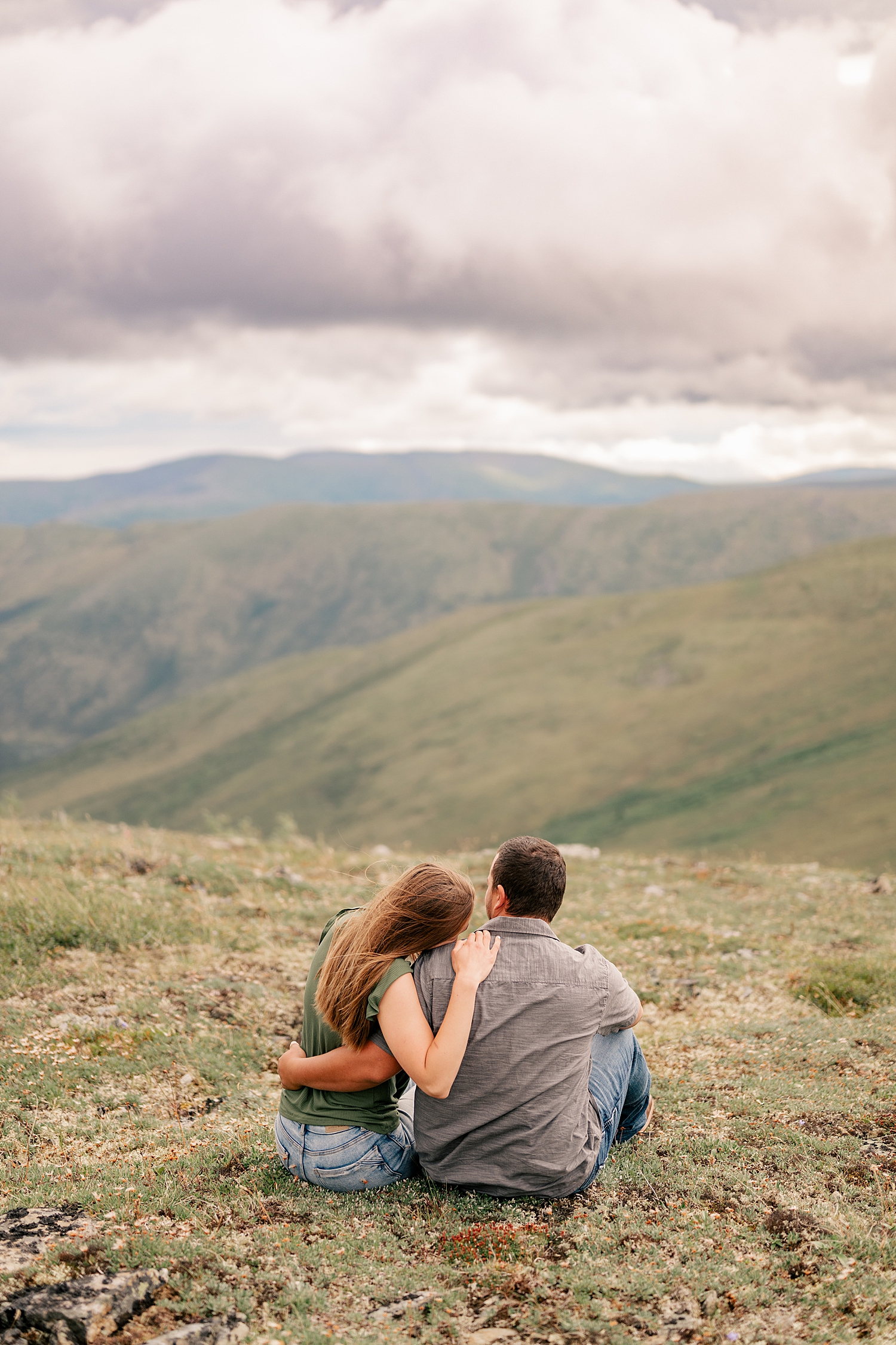man and woman sit on hillside enjoying the view for adventure engagement session in Alaska