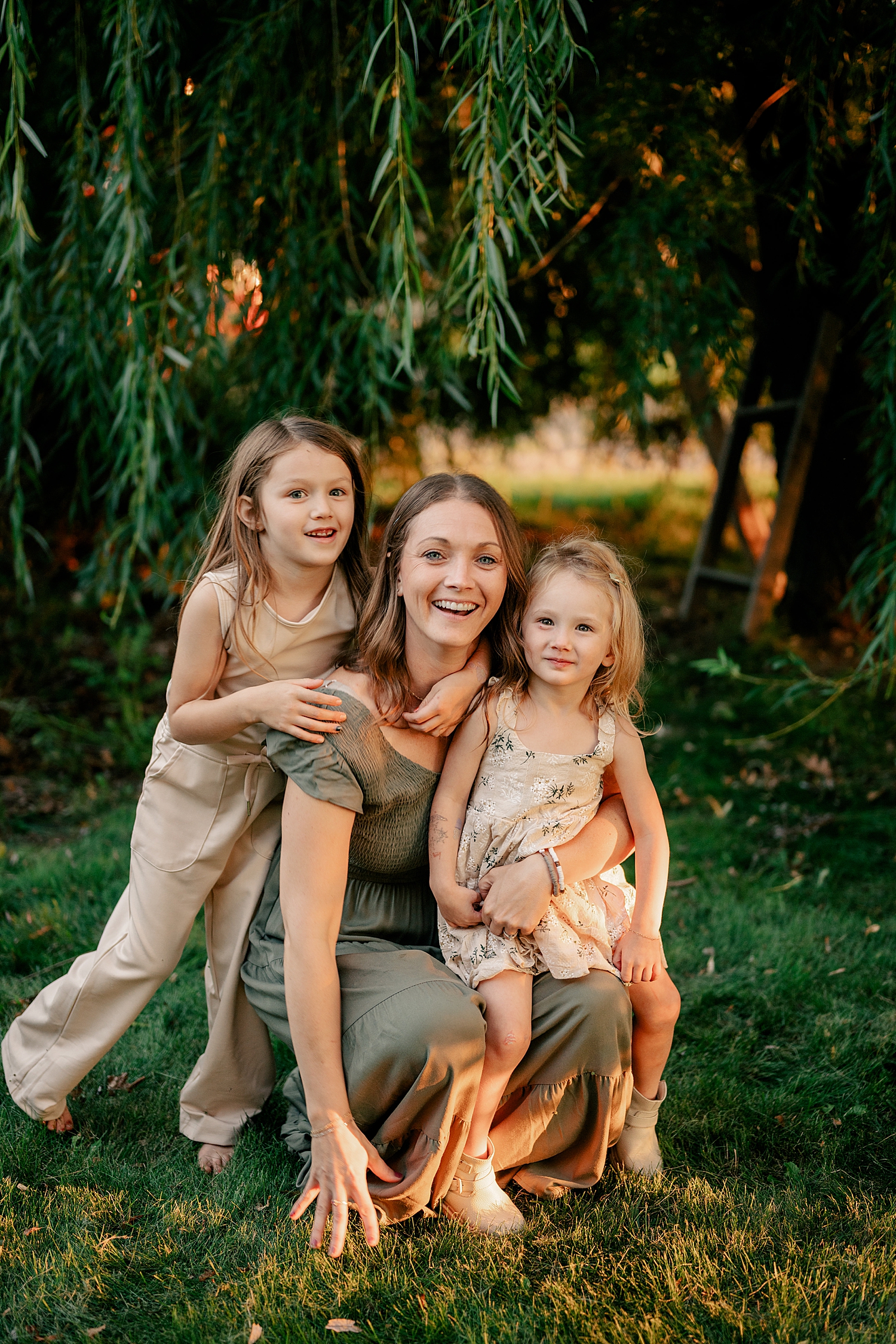 mom kneels in grass with two daughters for homegrown sessions