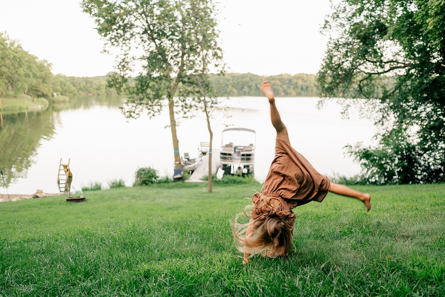 daughter does a cartwhel in the grass in front of water by Minnesota family photographer