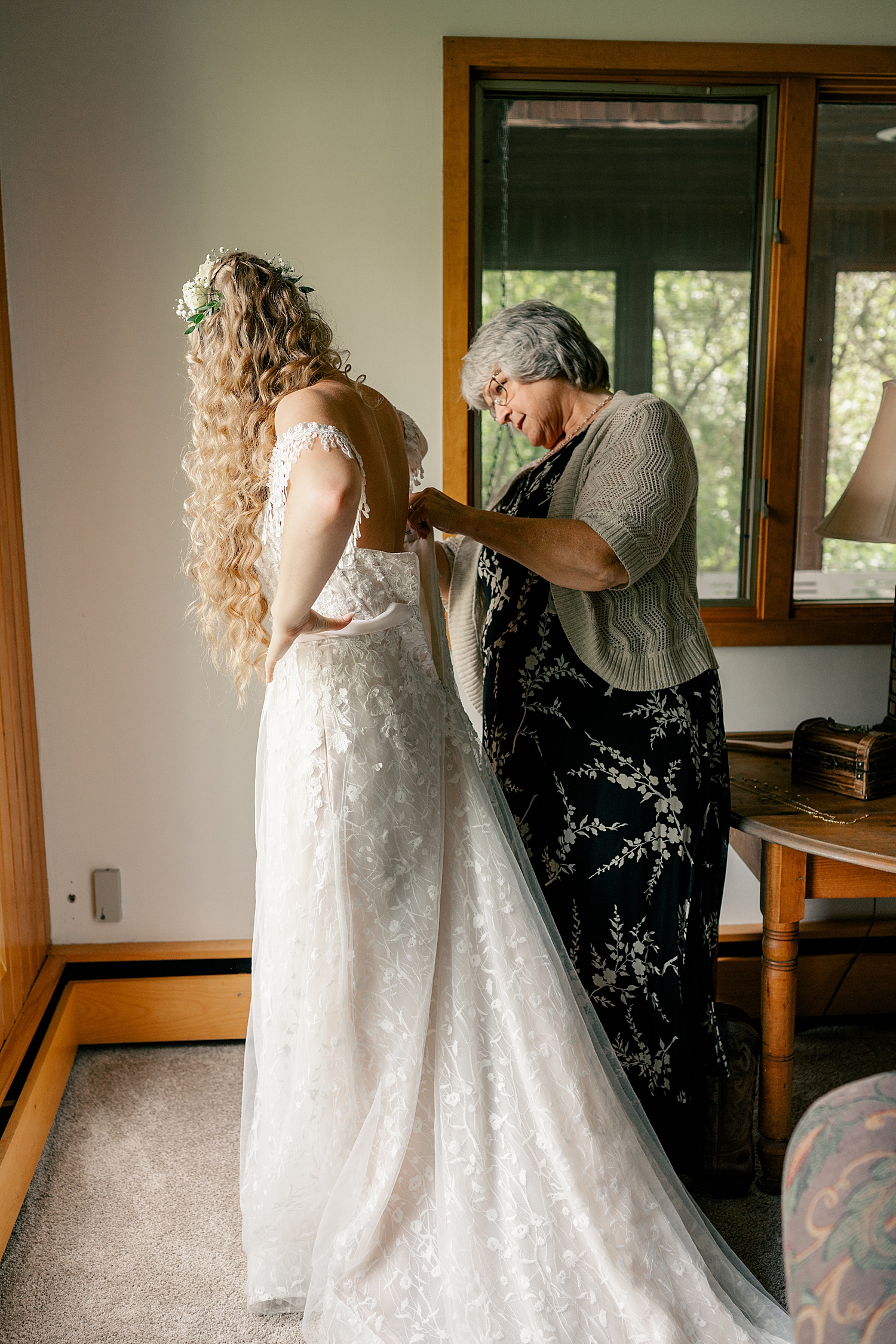 bride with curly blonde hair gets dressed buttoned by grandma at Gale Woods Farm