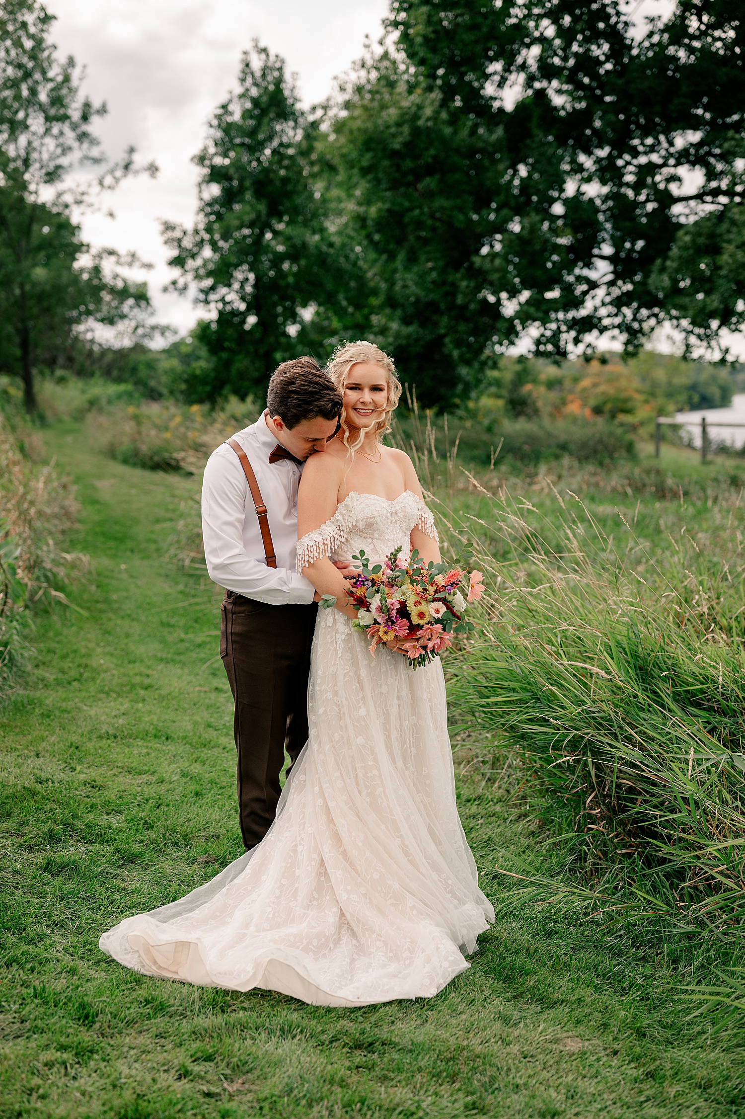man kisses woman's shoulder in a green field by Minnesota wedding photographer