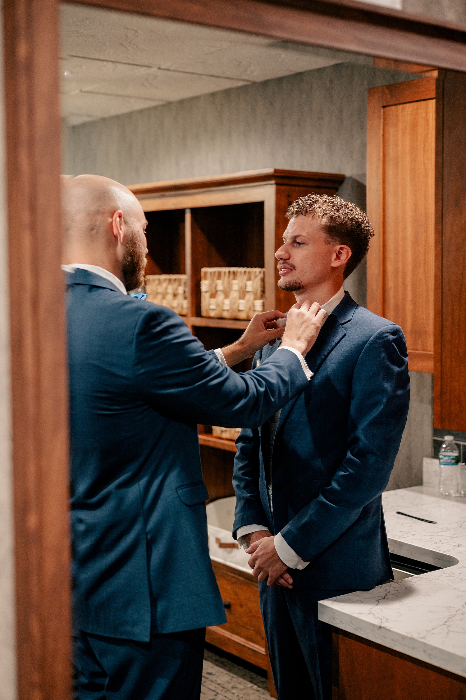 man adjusts his friend's bowtie before a big celebration by Minnesota wedding photographer