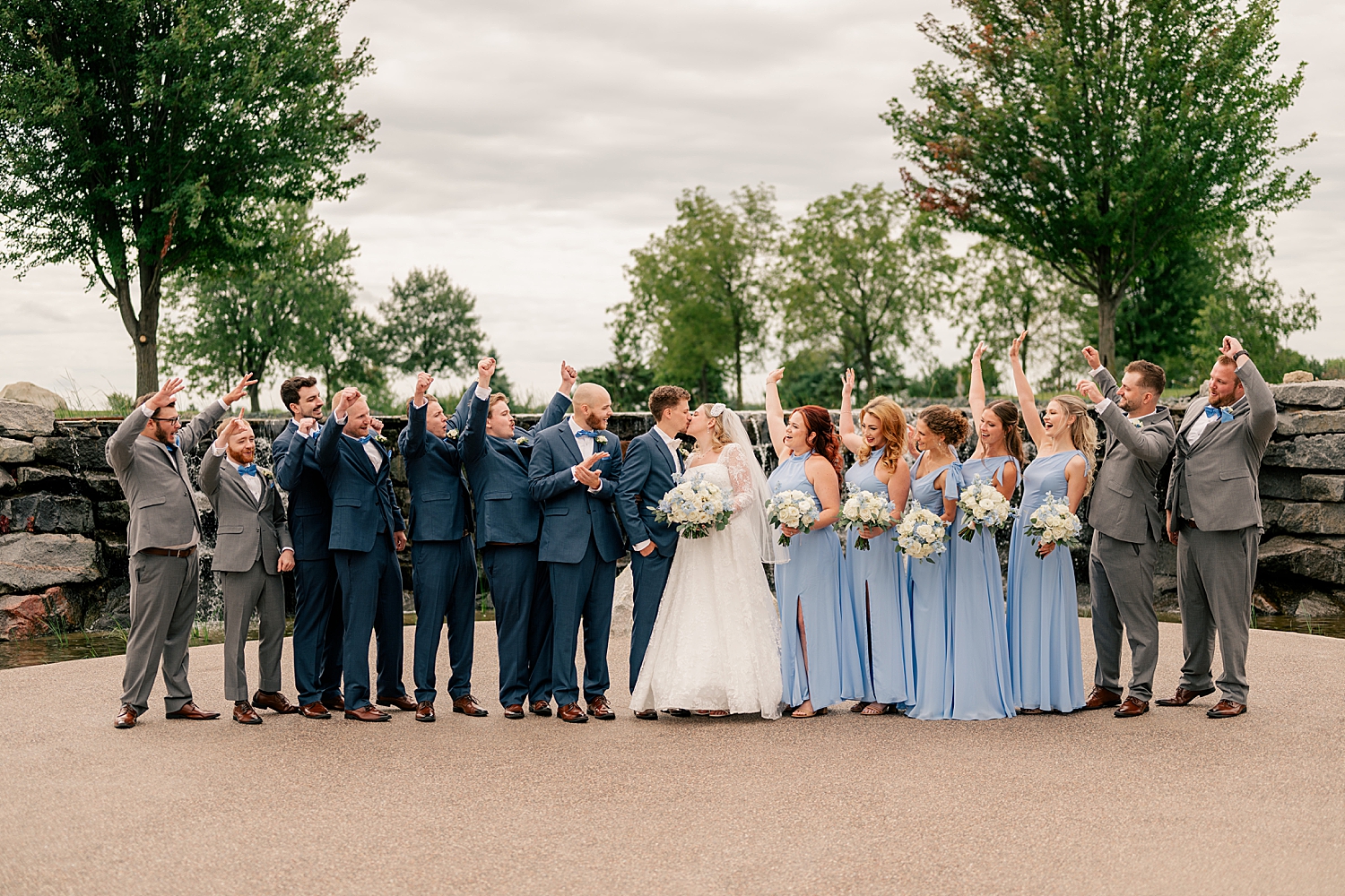 bridal party in pale and dark blue surround newlyweds by Minnesota wedding photographer