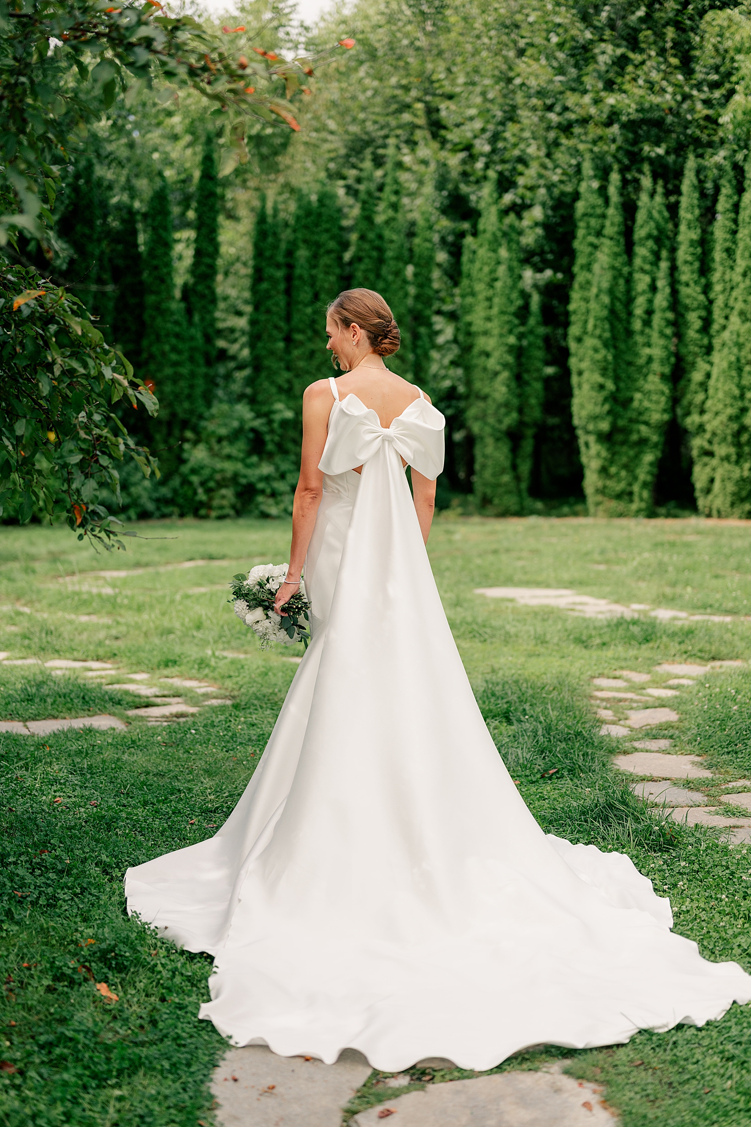 woman in long white dress with big bow in garden by Rule Creative Co
