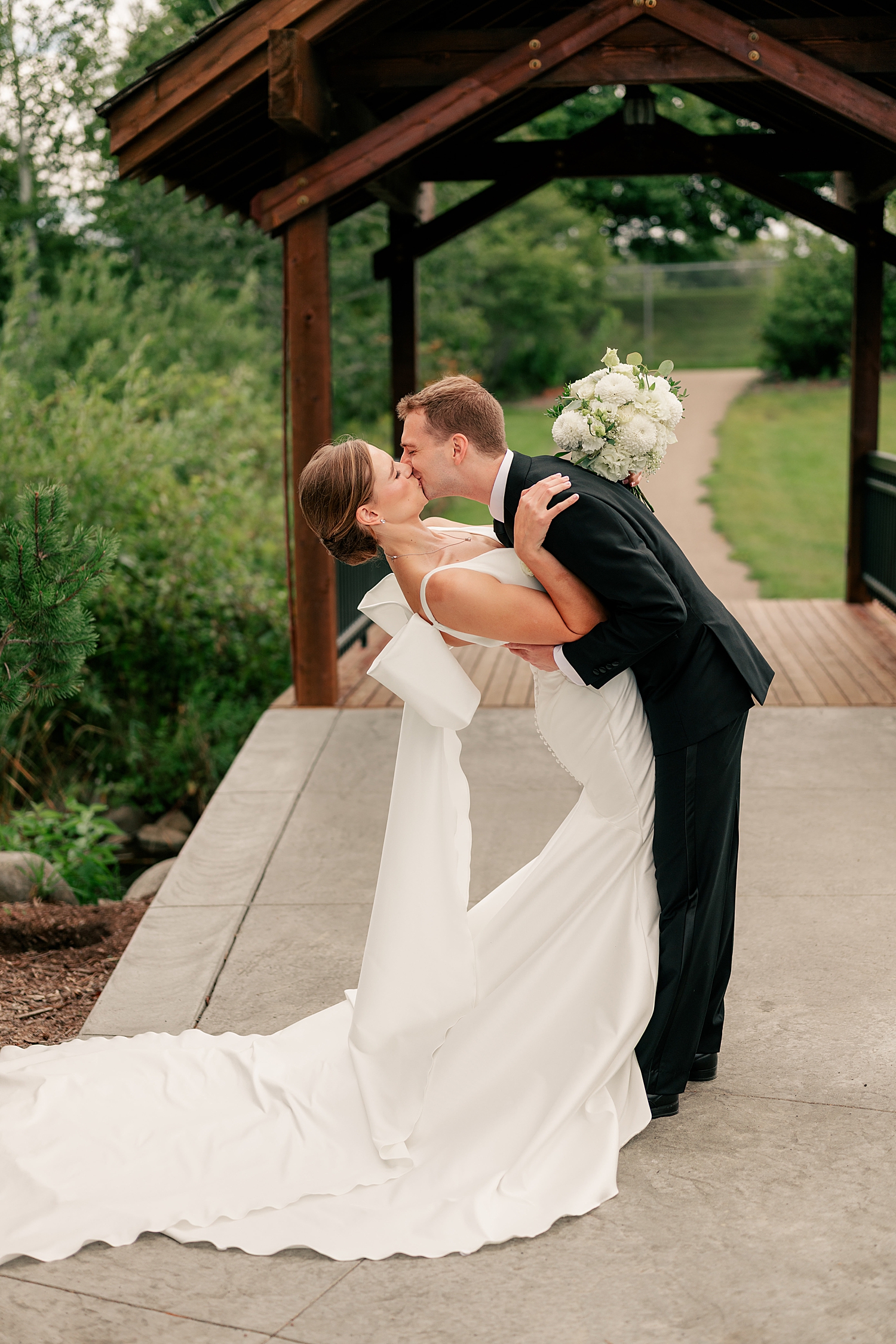 man dips woman in white dress for a kiss on bridge by Rule Creative Co
