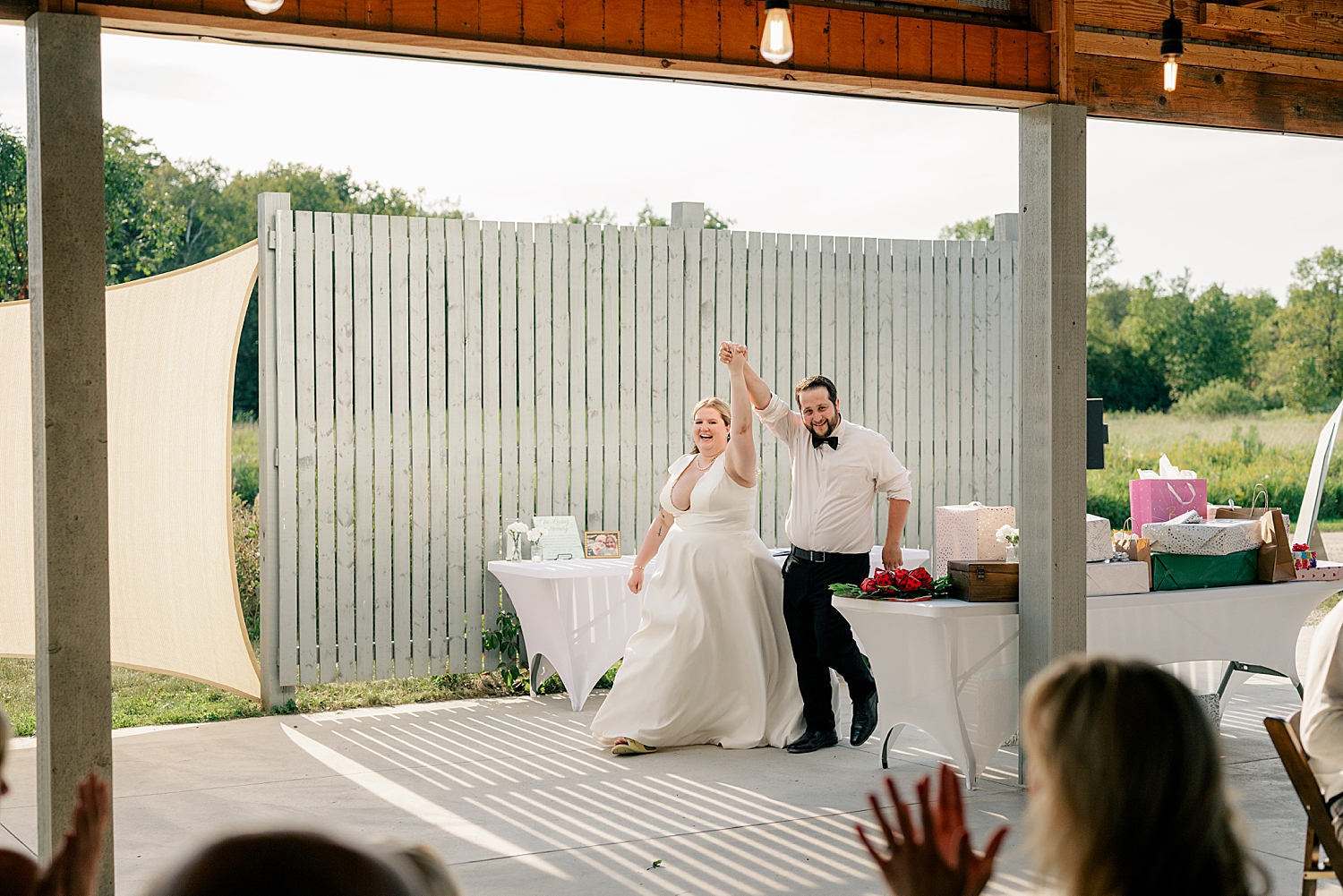 newlyweds hold up hands as they enter the pavilion reception for August Minnesota Wedding