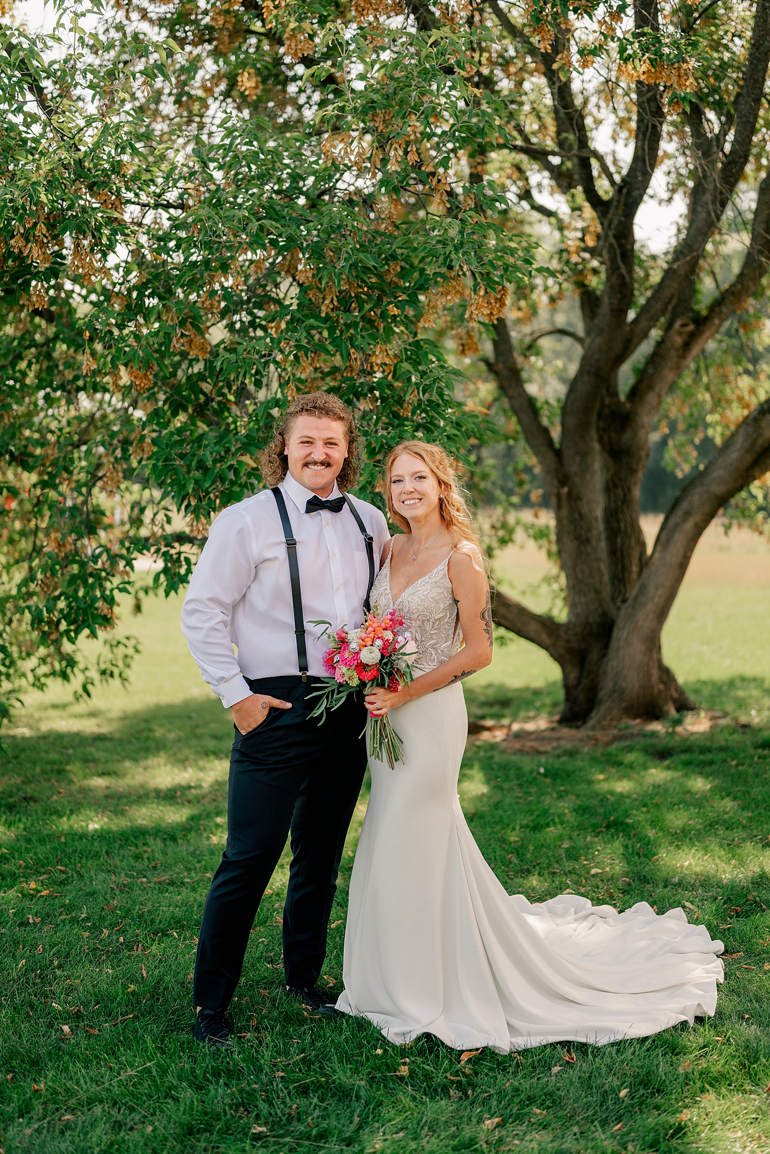 husband and wife stand under tree grinning by Rule Creative Co