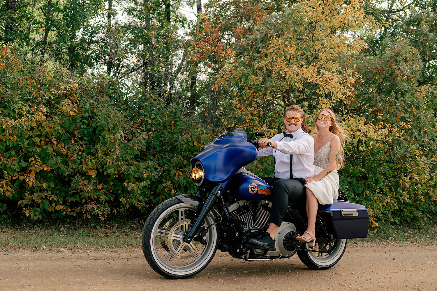 newlyweds grin on the back of blue motorcycle at Red Oak Farm
