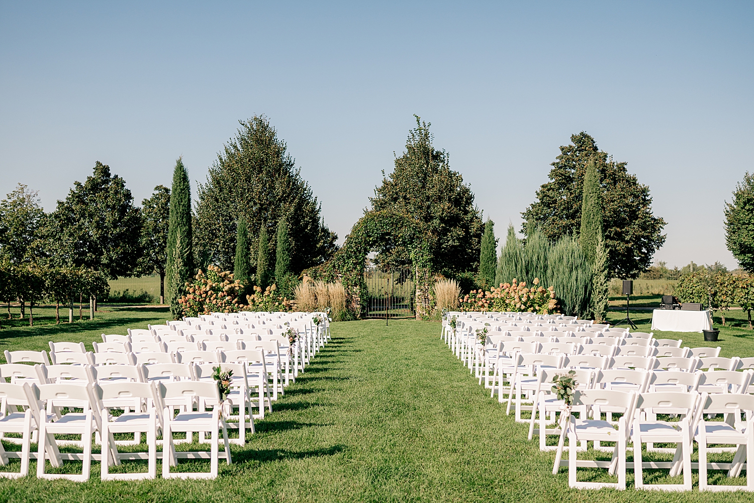 large outdoor ceremony space set up on lawn with white chairs by Minnesota wedding photographer