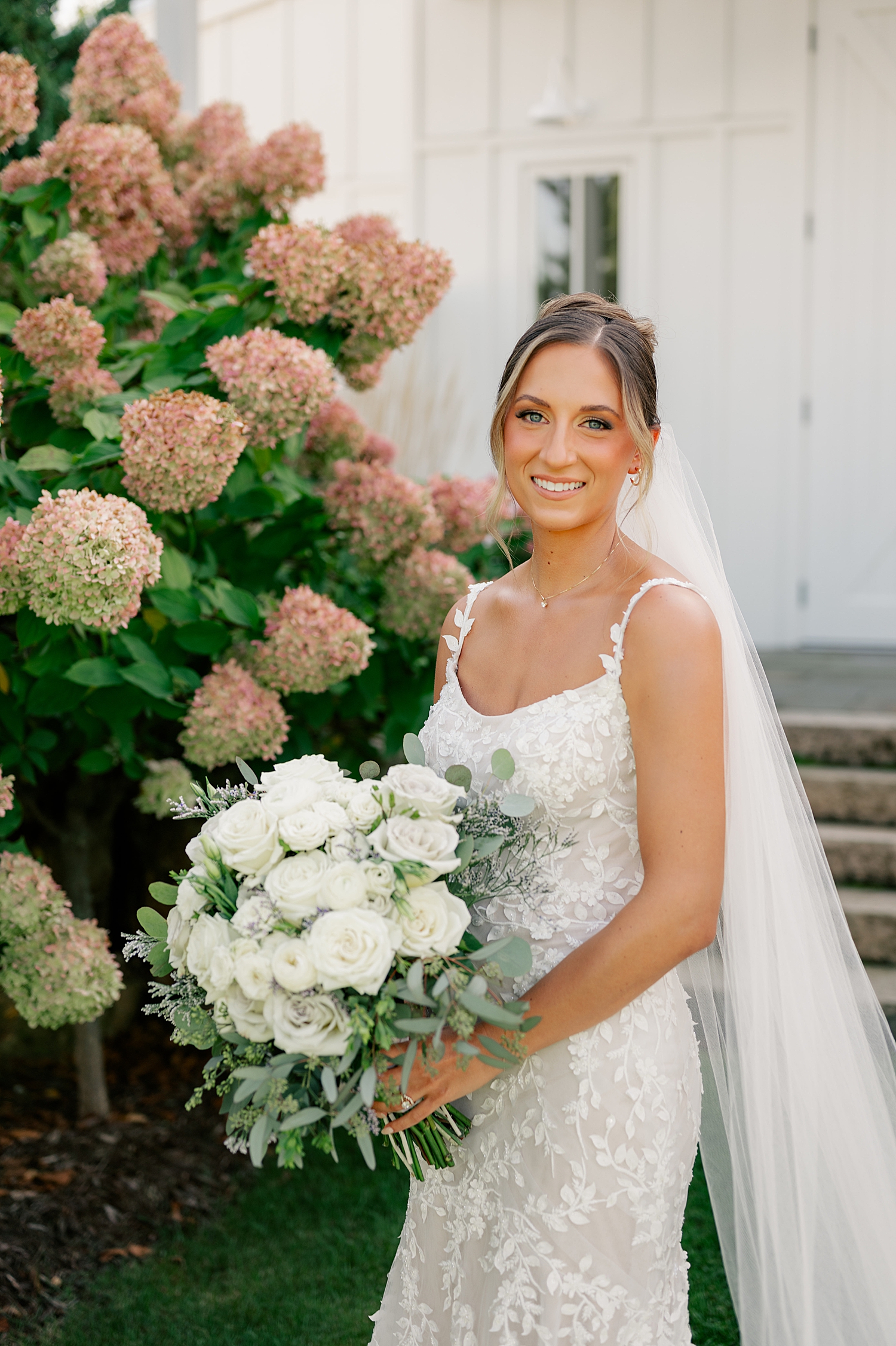 blonde woman in long bridal gown in front of pink hydrangeas at Redeemed Farm