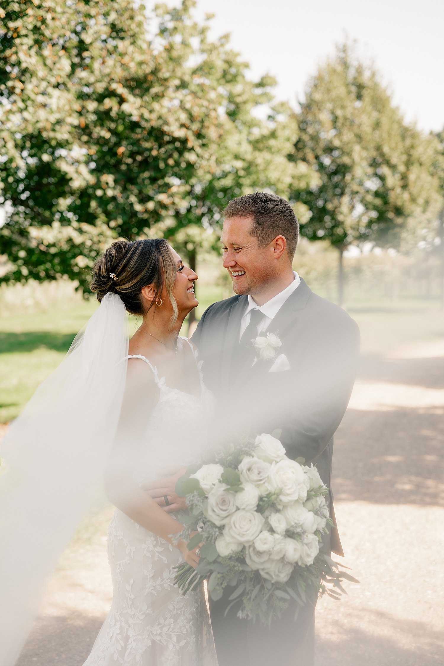 newlyweds laugh together wrapped up in veil at Redeemed Farm