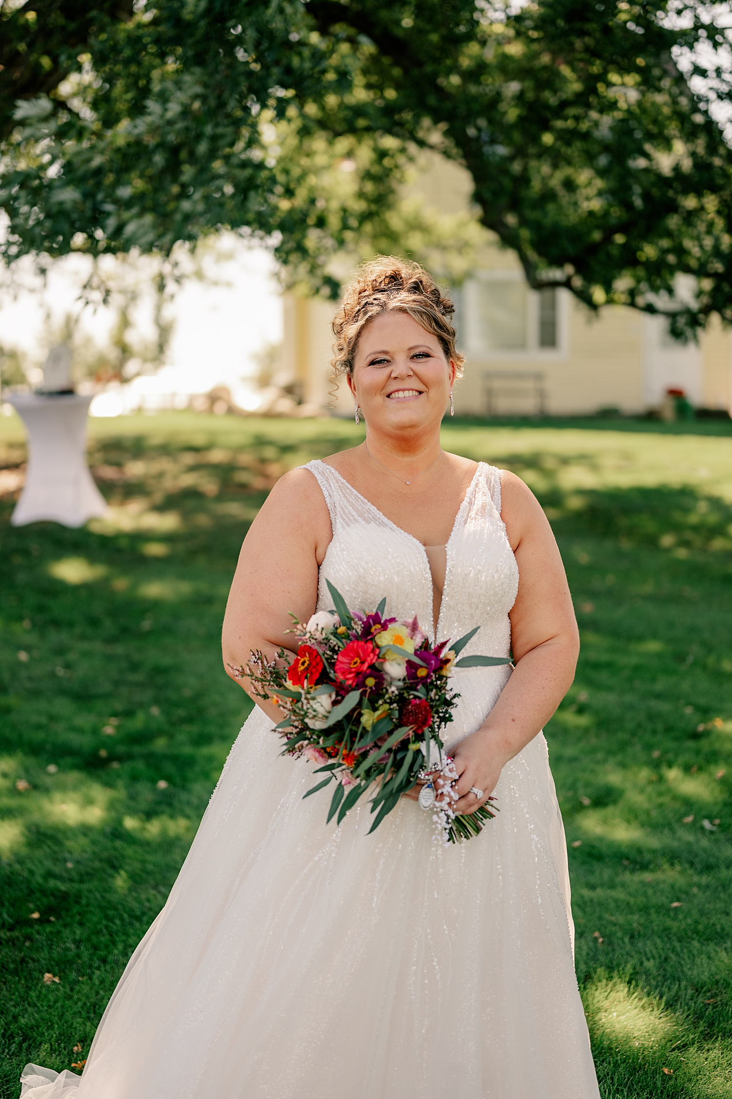 blond bride stands in shade under tree by Minnesota wedding photographer