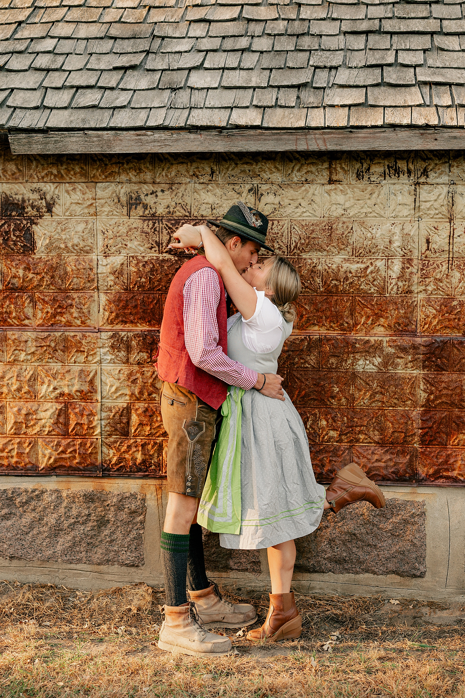 man and woman in German clothing kiss outside house by Rule Creative Co