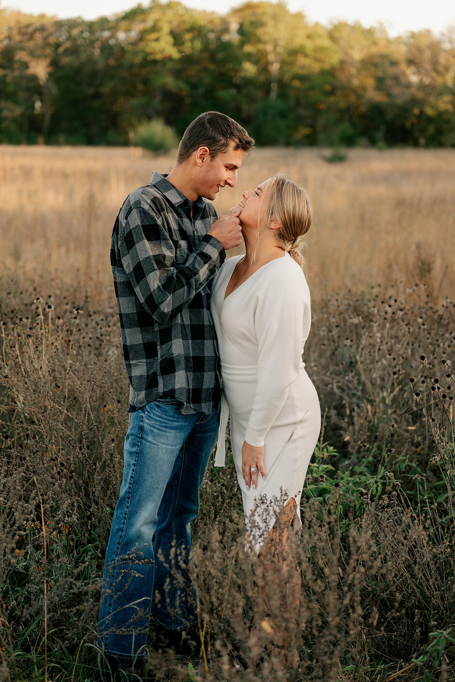 bonde in a white dress leans up to kiss man in field for sunset engagement session