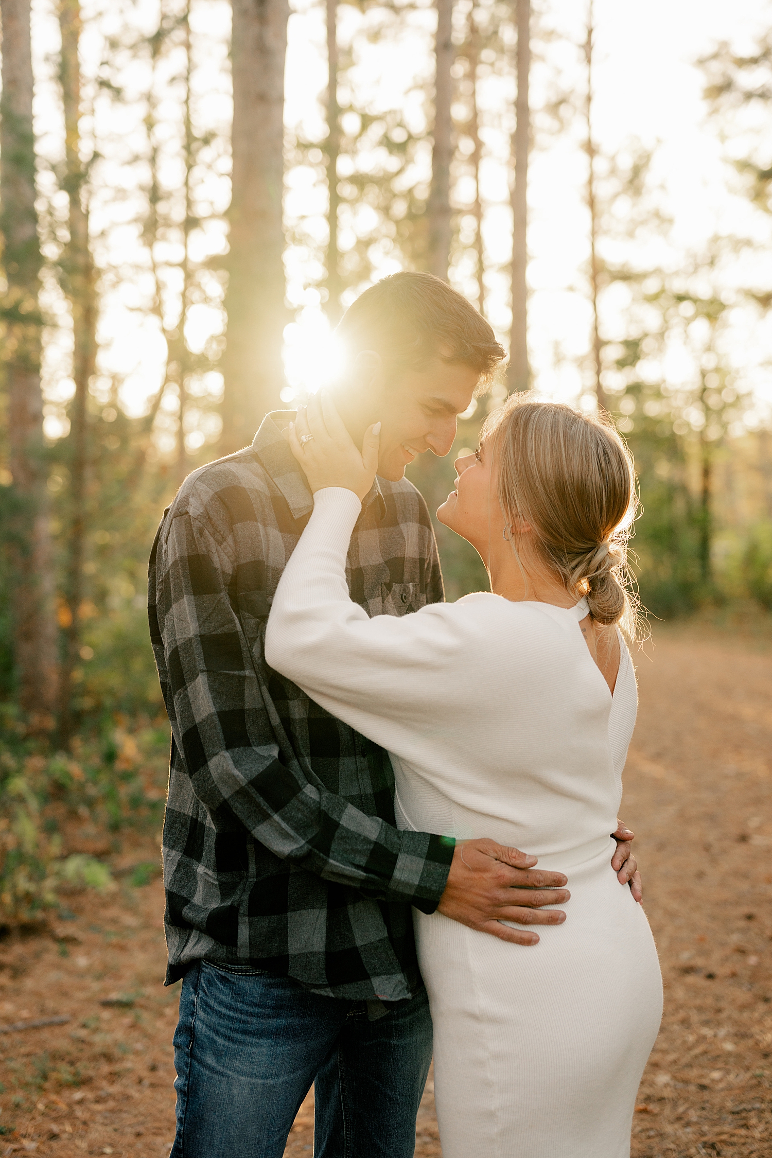 couple embrace under golden light in the forest for sunset engagement session