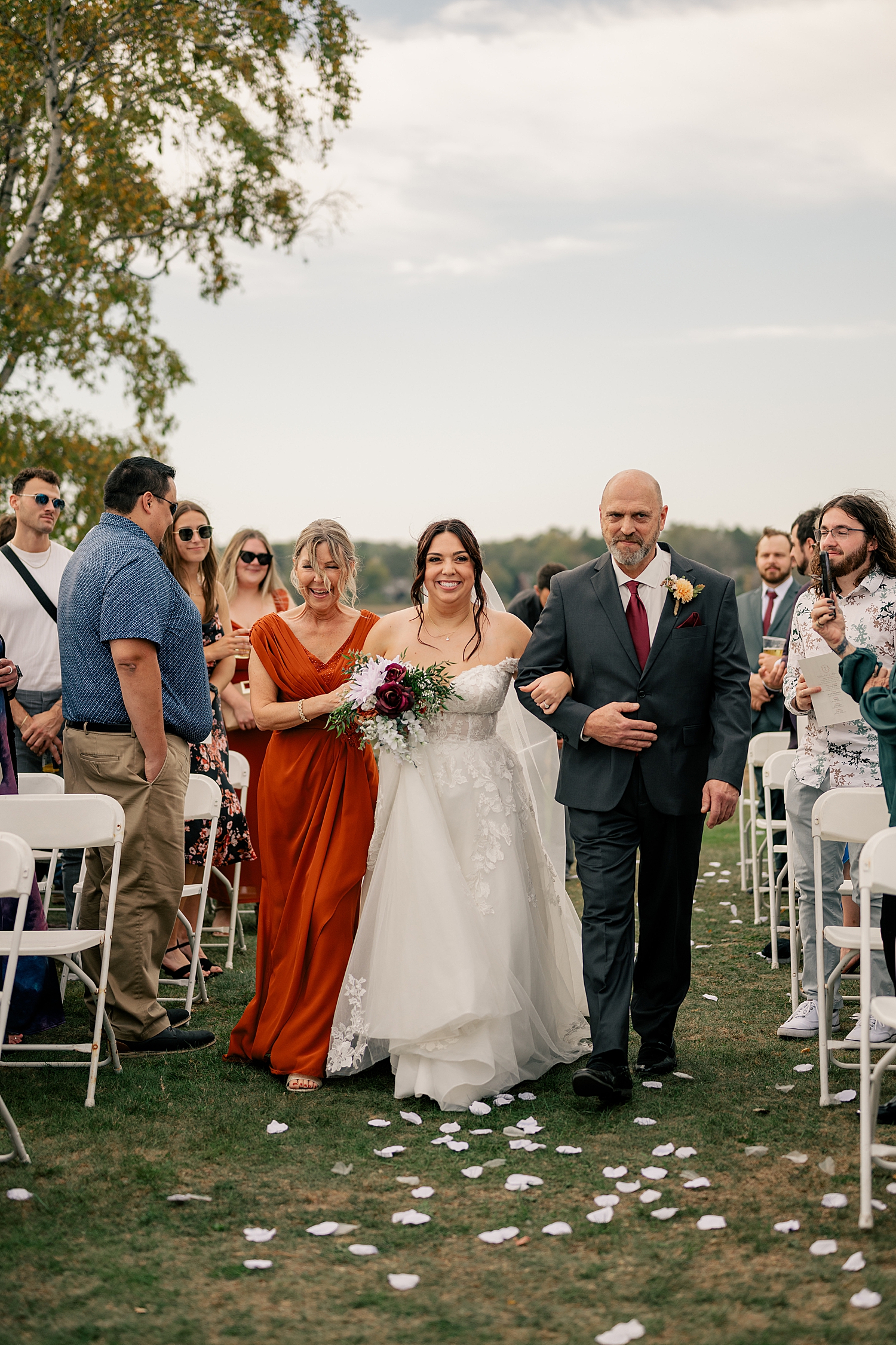bride walks down outdoor aisle with both parents at Breezy Point venue