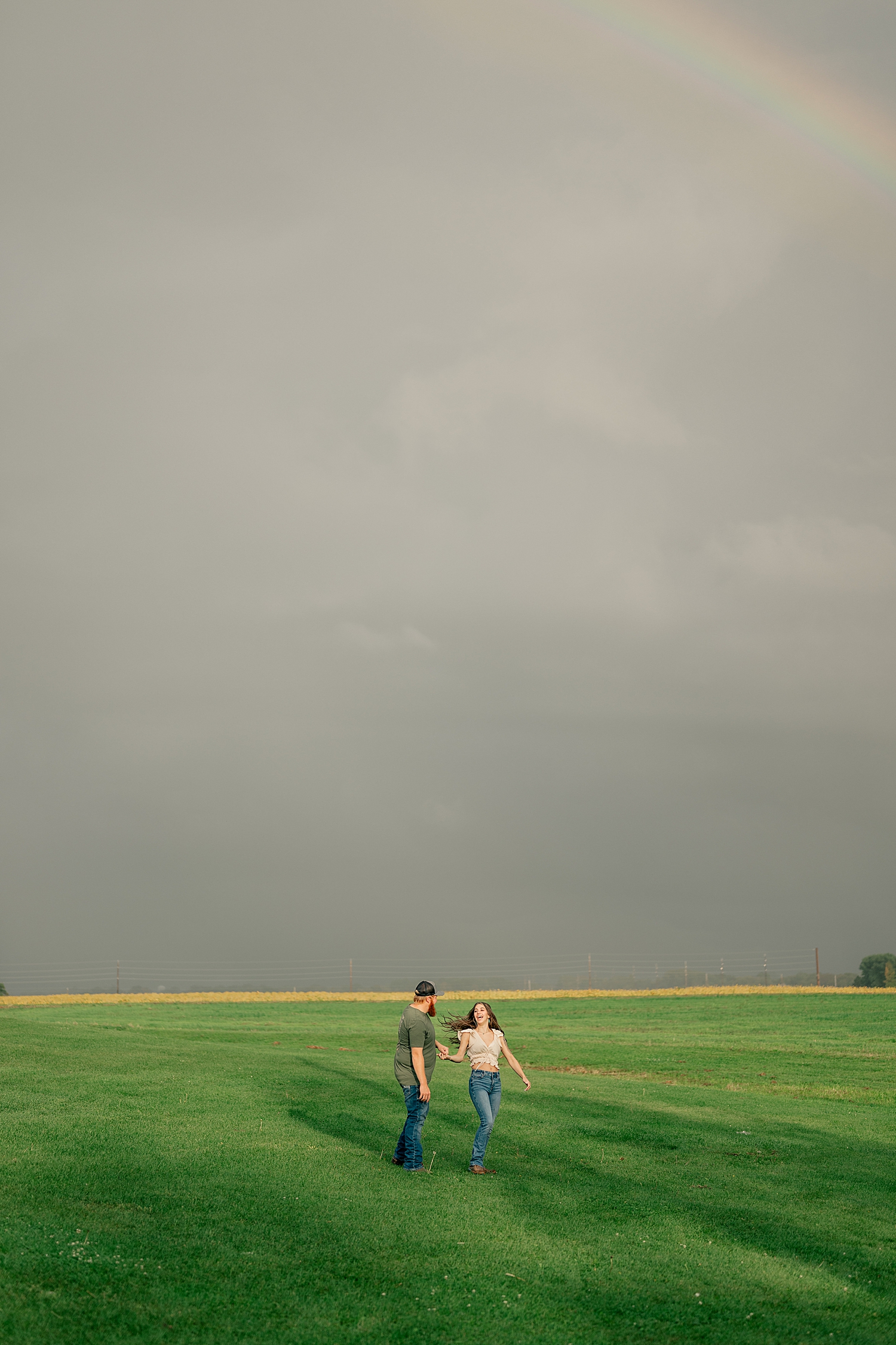 two people dance in green lawn under stormy skies for double rainbow engagement session