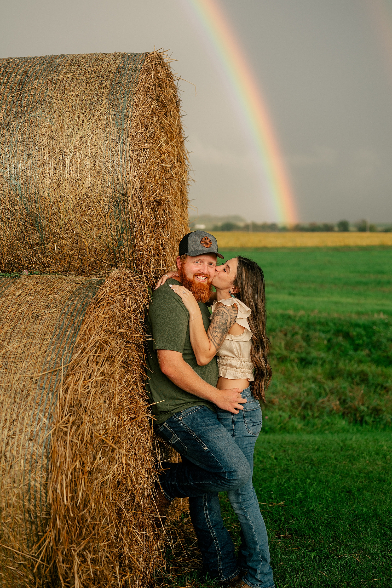 bride to be kisses her man under dark sky for double rainbow engagement session