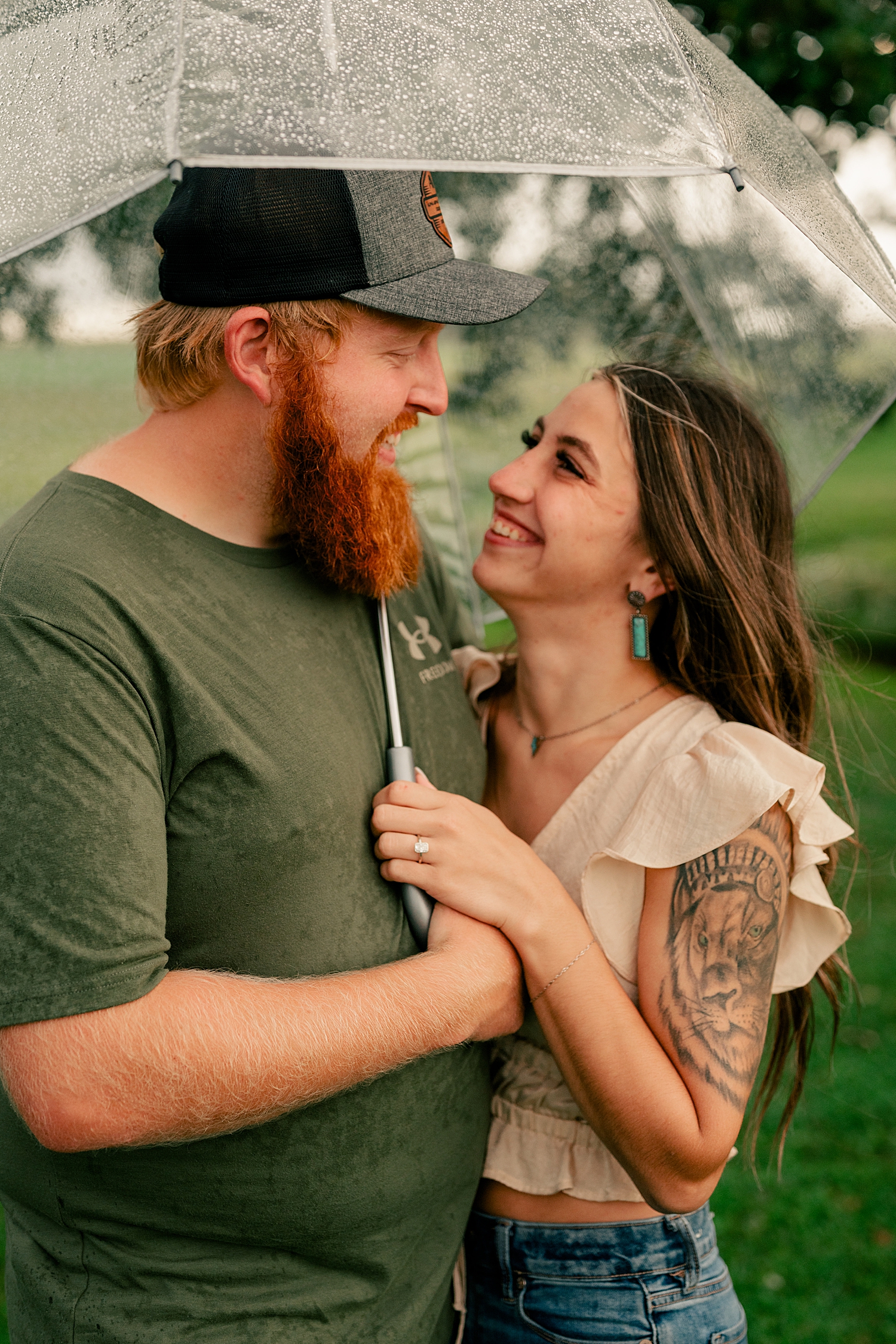couple snuggle under clear umbrella for double rainbow engagement session