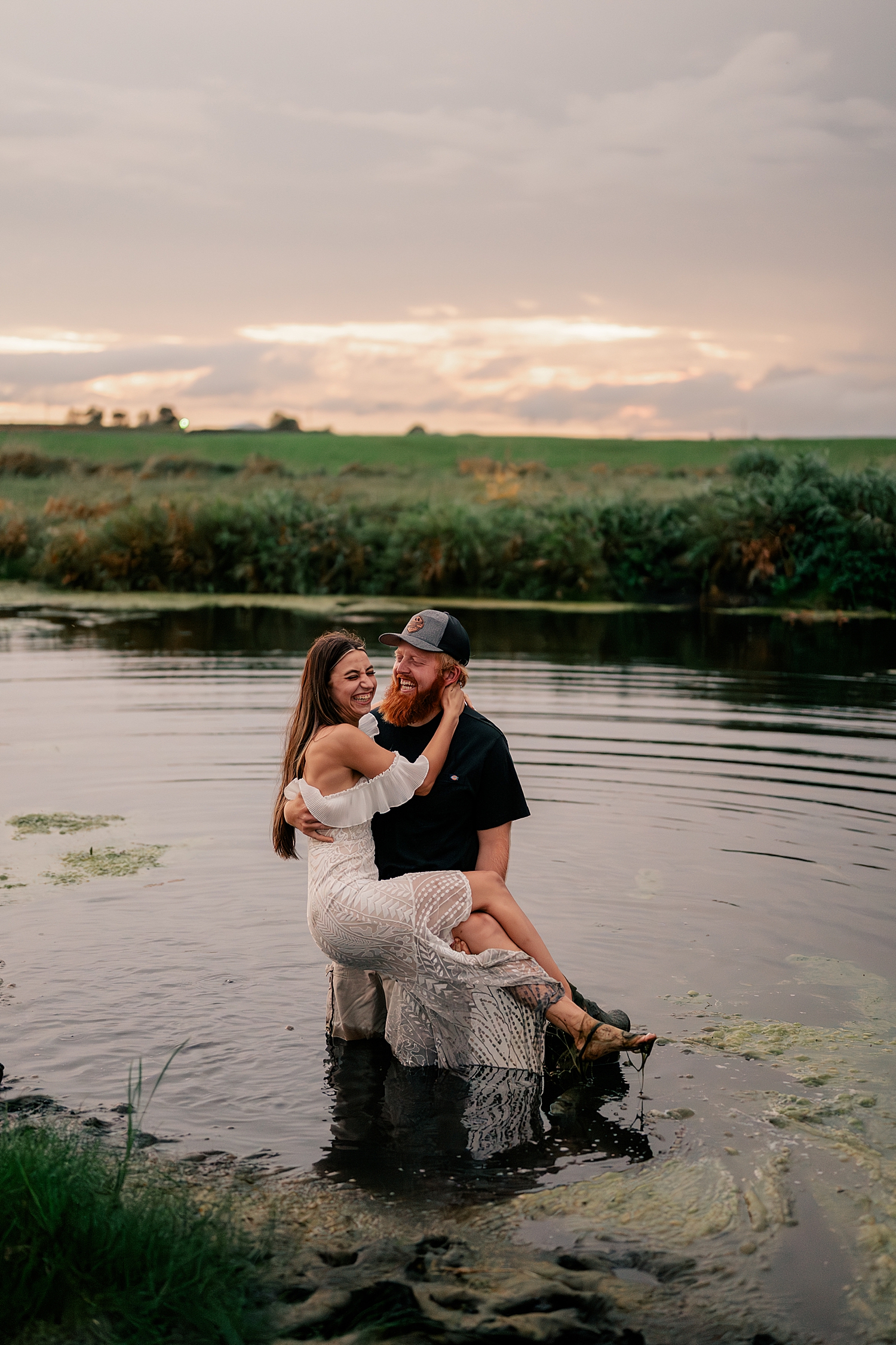redhead man holds up bride to be in pond by Rule Creative Co