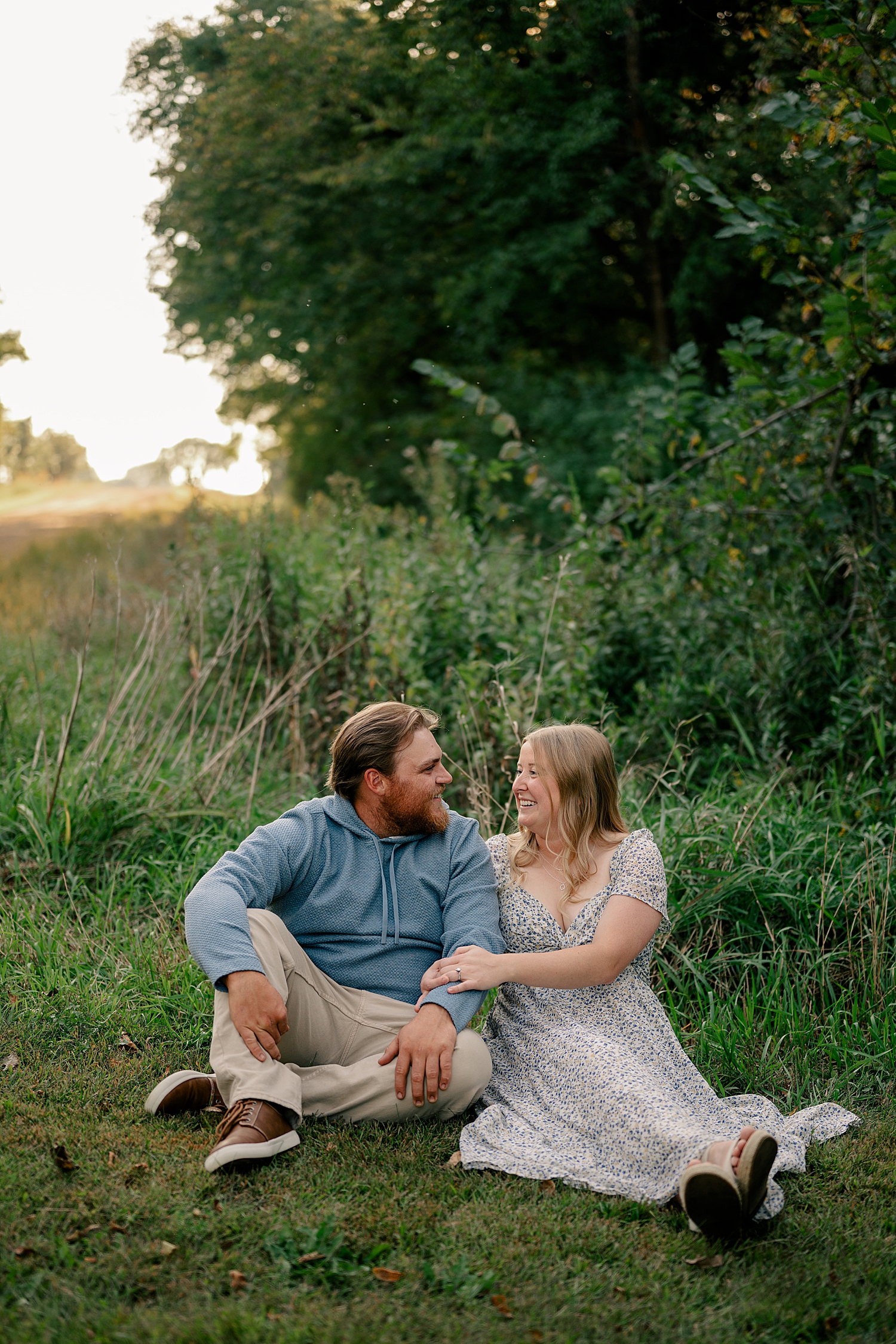 two people sit in the grass under tall green trees by Minnesota wedding photographer