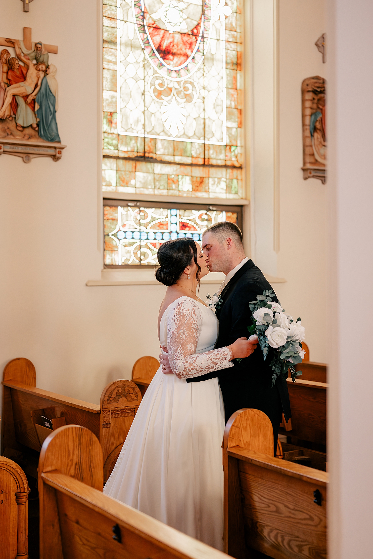 couple shares a kiss in pew under stained glass by Rule Creative Co