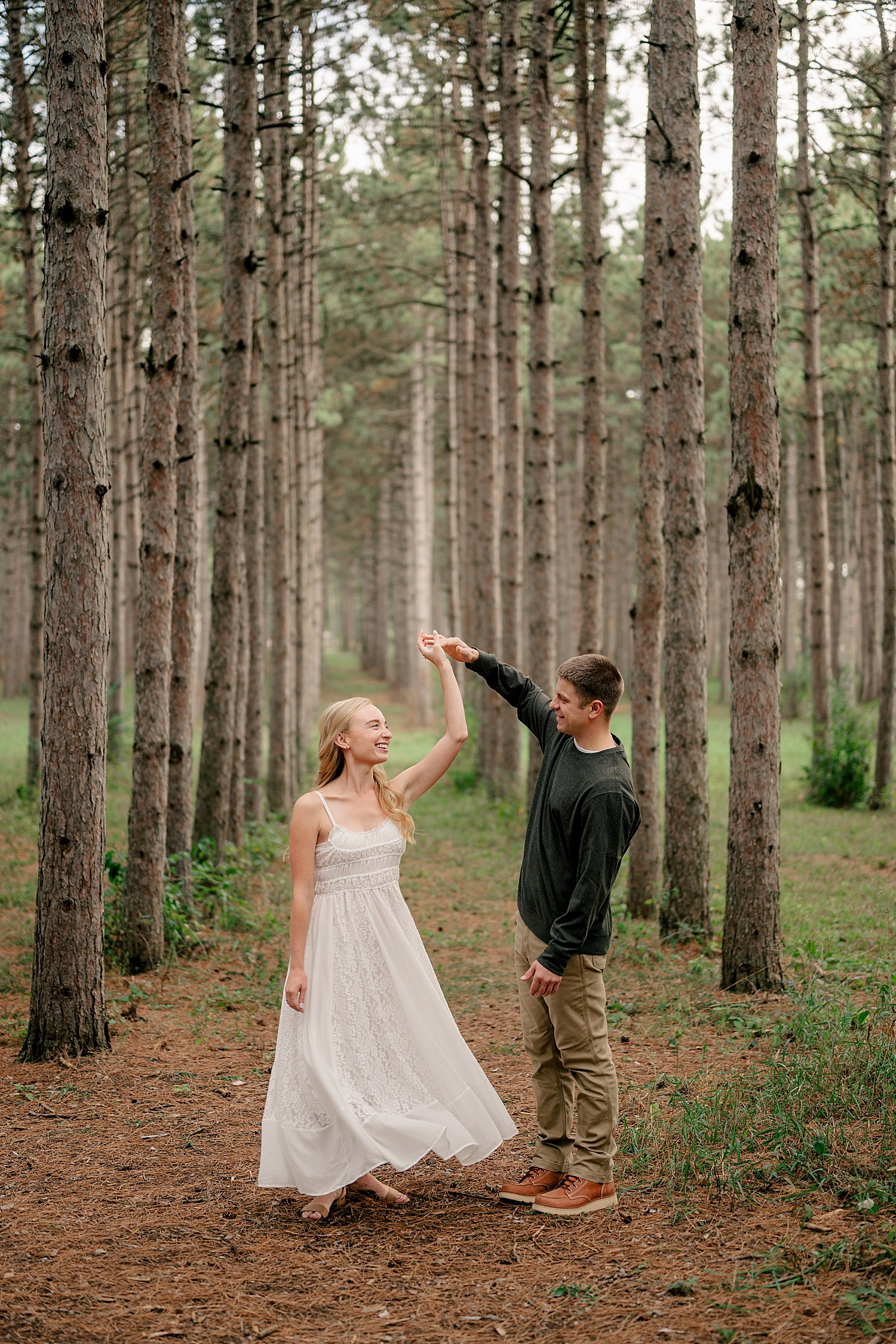 groom-to-be twirls lady in white dress in trees by Minnesota wedding photographer