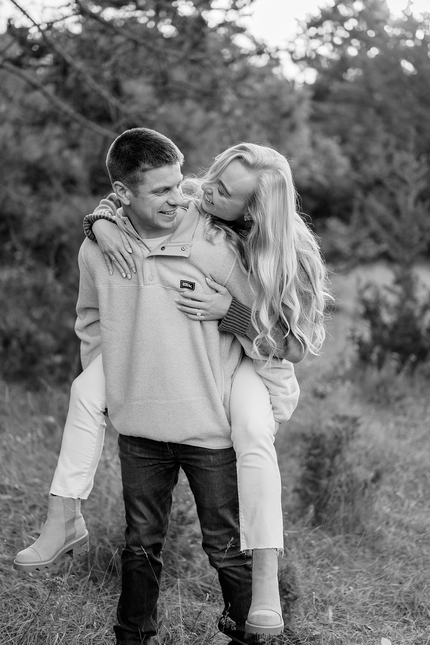 blonde jumps on man's back in field by Minnesota wedding photographer