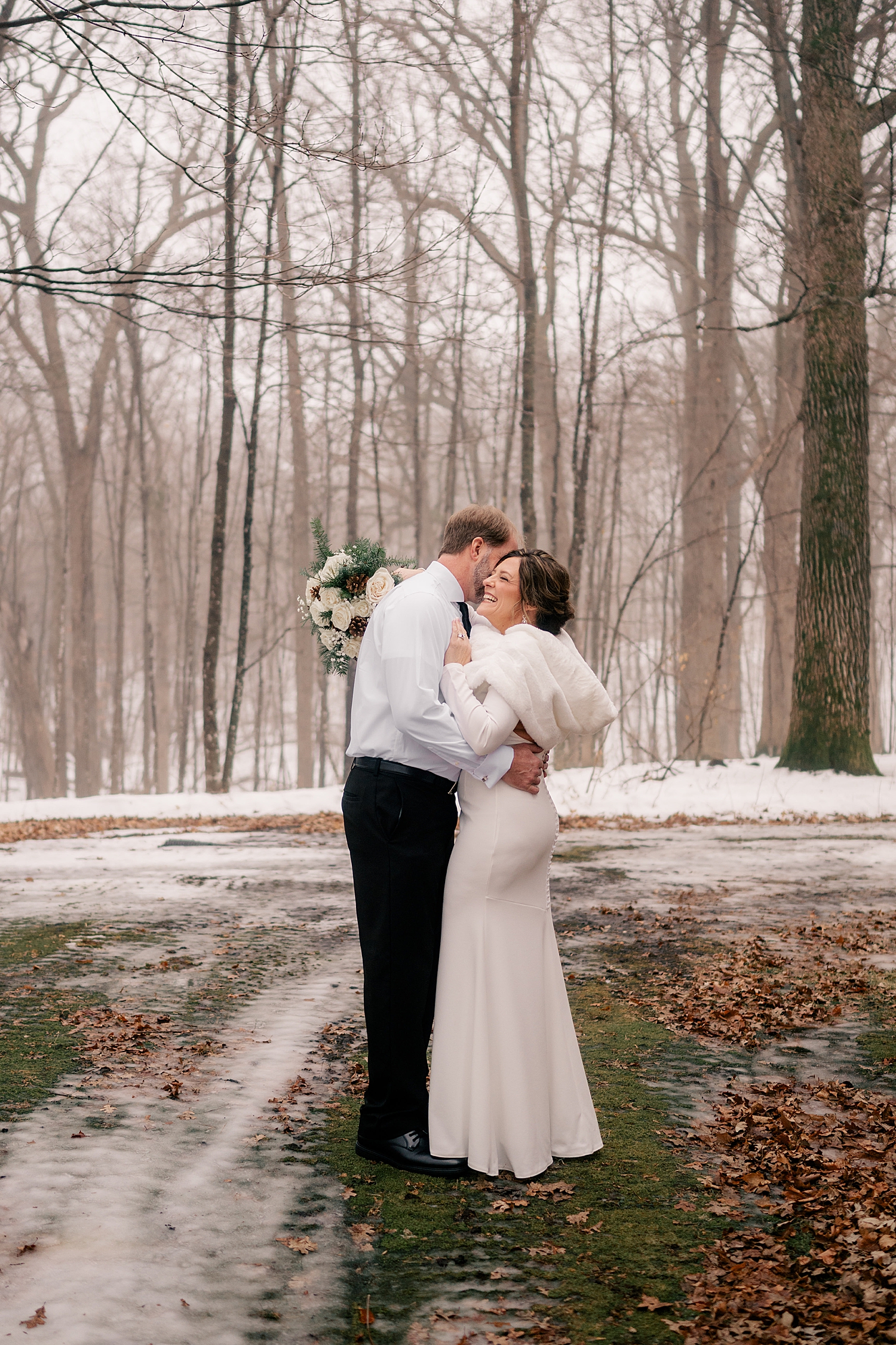 man and woman embrace in cold field surrounded by trees by Rule Creative Co