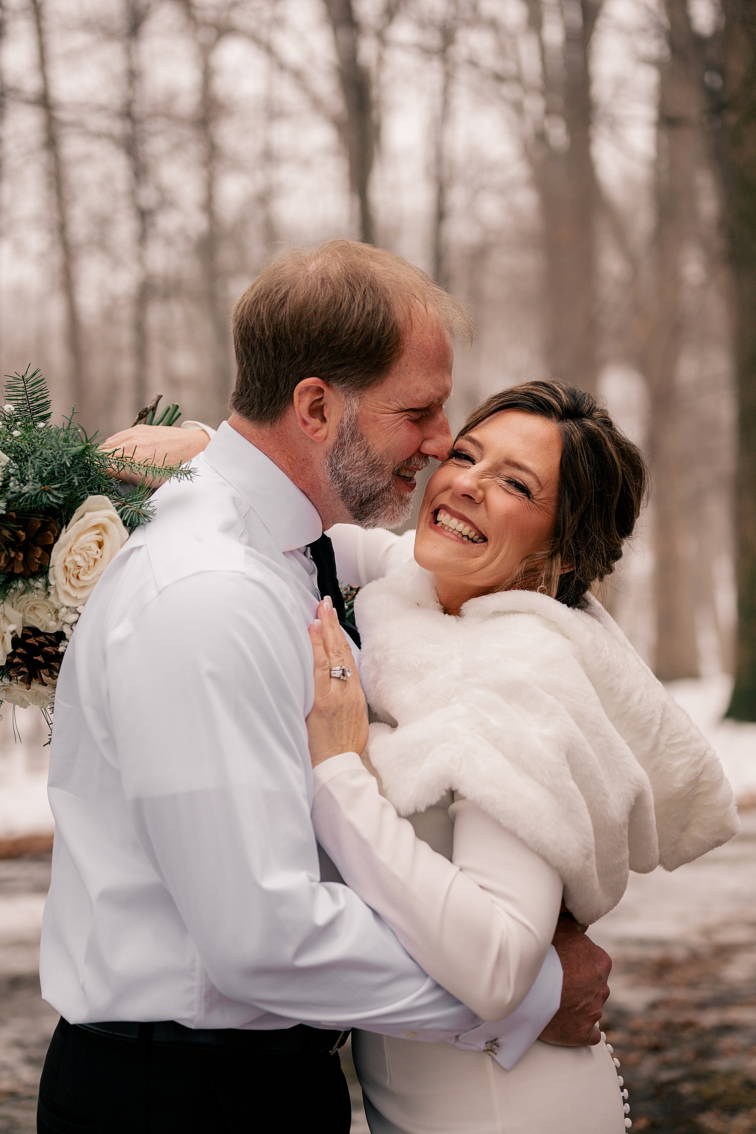 bride and groom giggle together in snowy trees after learning how to keep your elopement personal