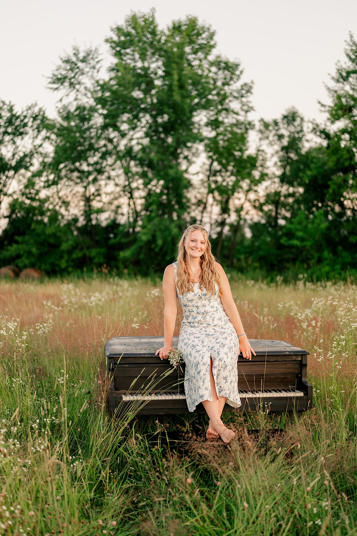 blonde in dress sits on instrument for Senior Photos with a Piano