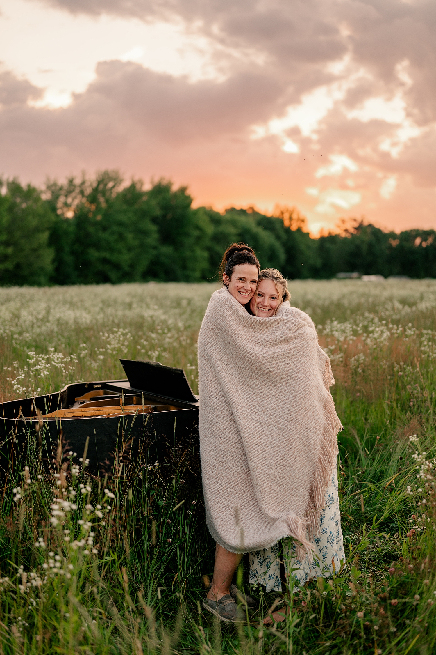 mother and daughter wrap up in a blanket in field by Rule Creative Co