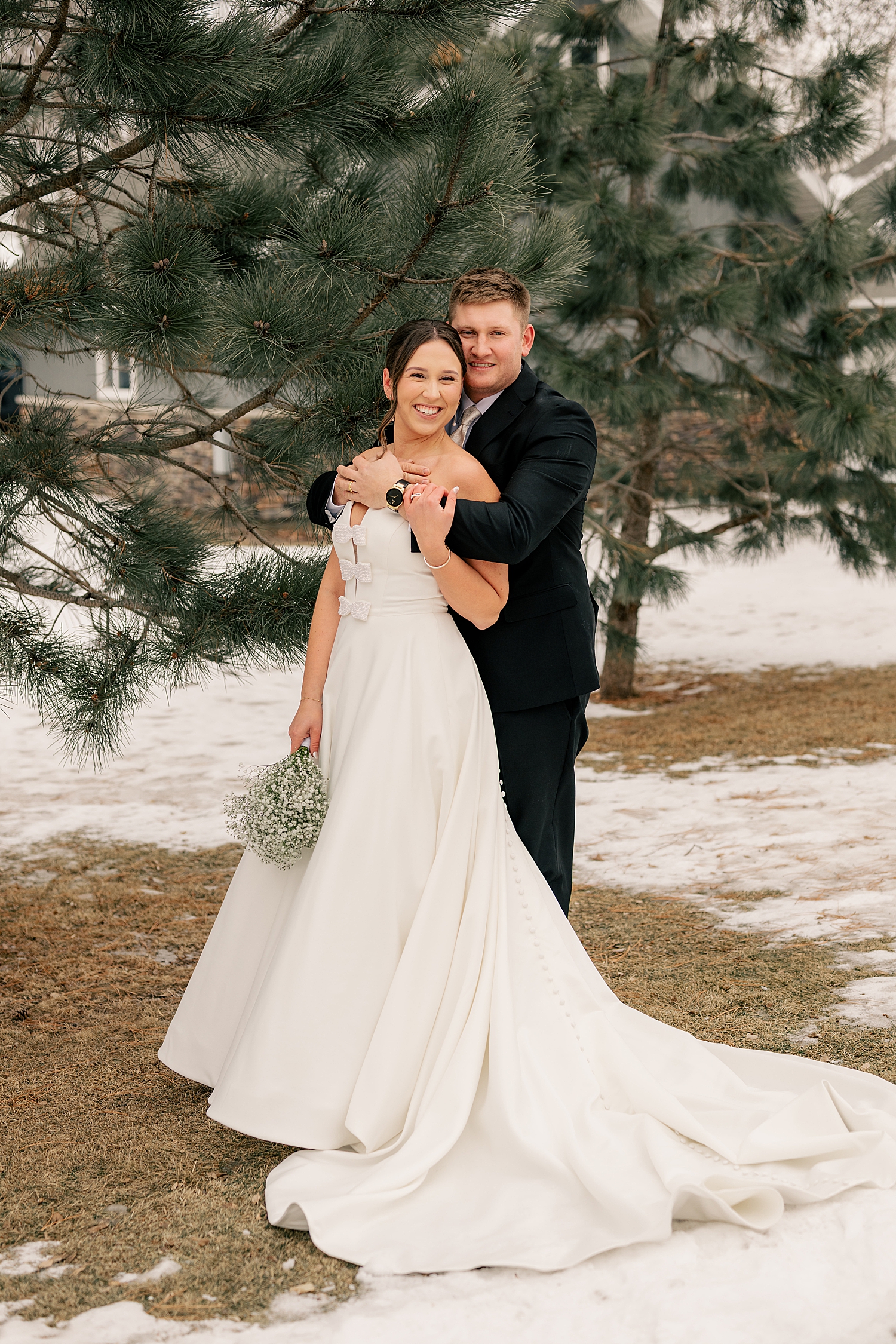 newlyweds stand in front of pine trees on the snow by Rule Creative Co